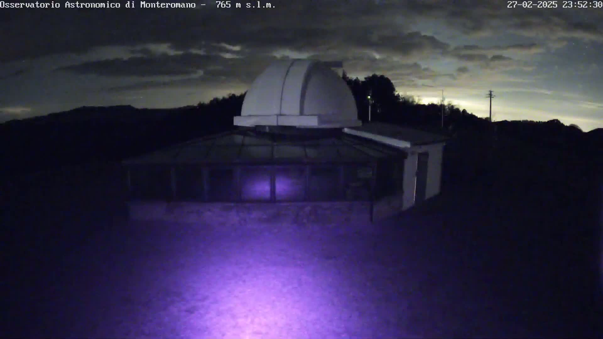 A nighttime view of an observatory building with a dome under a partly cloudy sky.