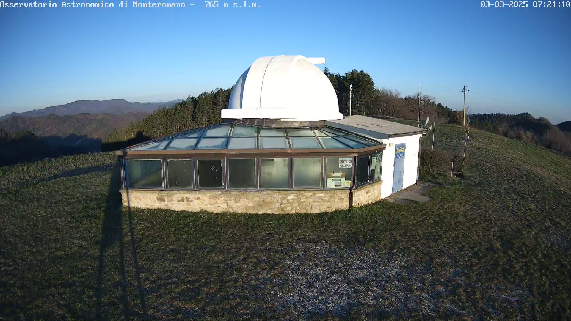 A white-domed observatory building with a glass sunroom sits on a grassy hilltop under a clear blue sky.