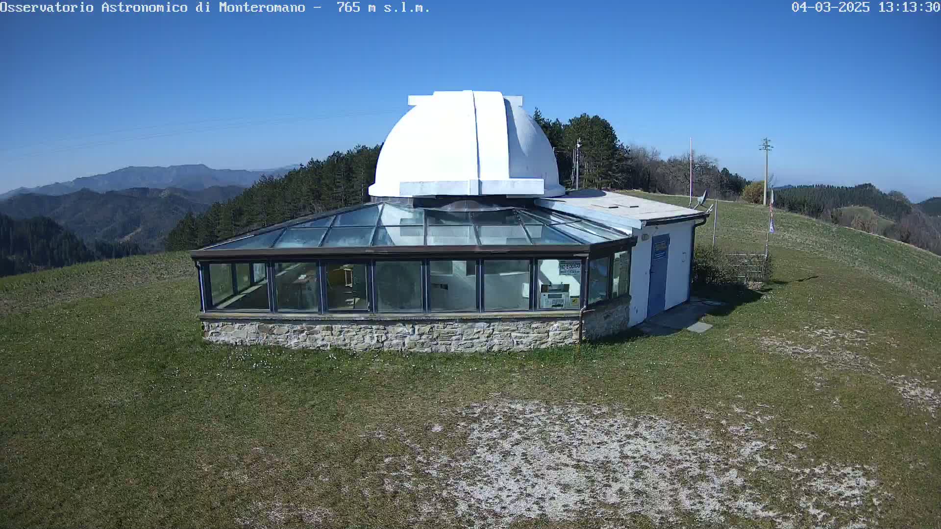 A white-domed observatory building with a glass enclosure sits on a grassy hilltop under a clear blue sky.