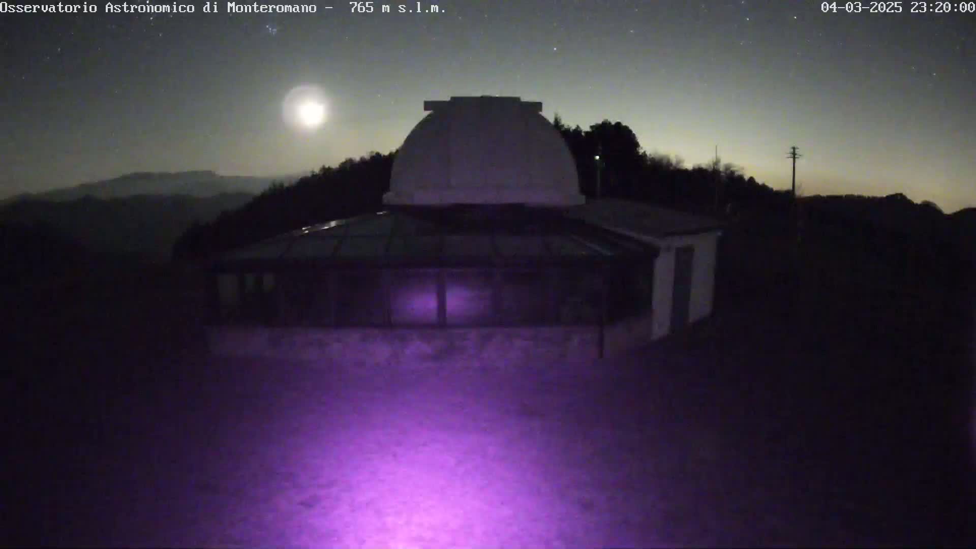 A nighttime image shows a building with a dome, surrounded by trees under a clear, starry sky with a bright moon.