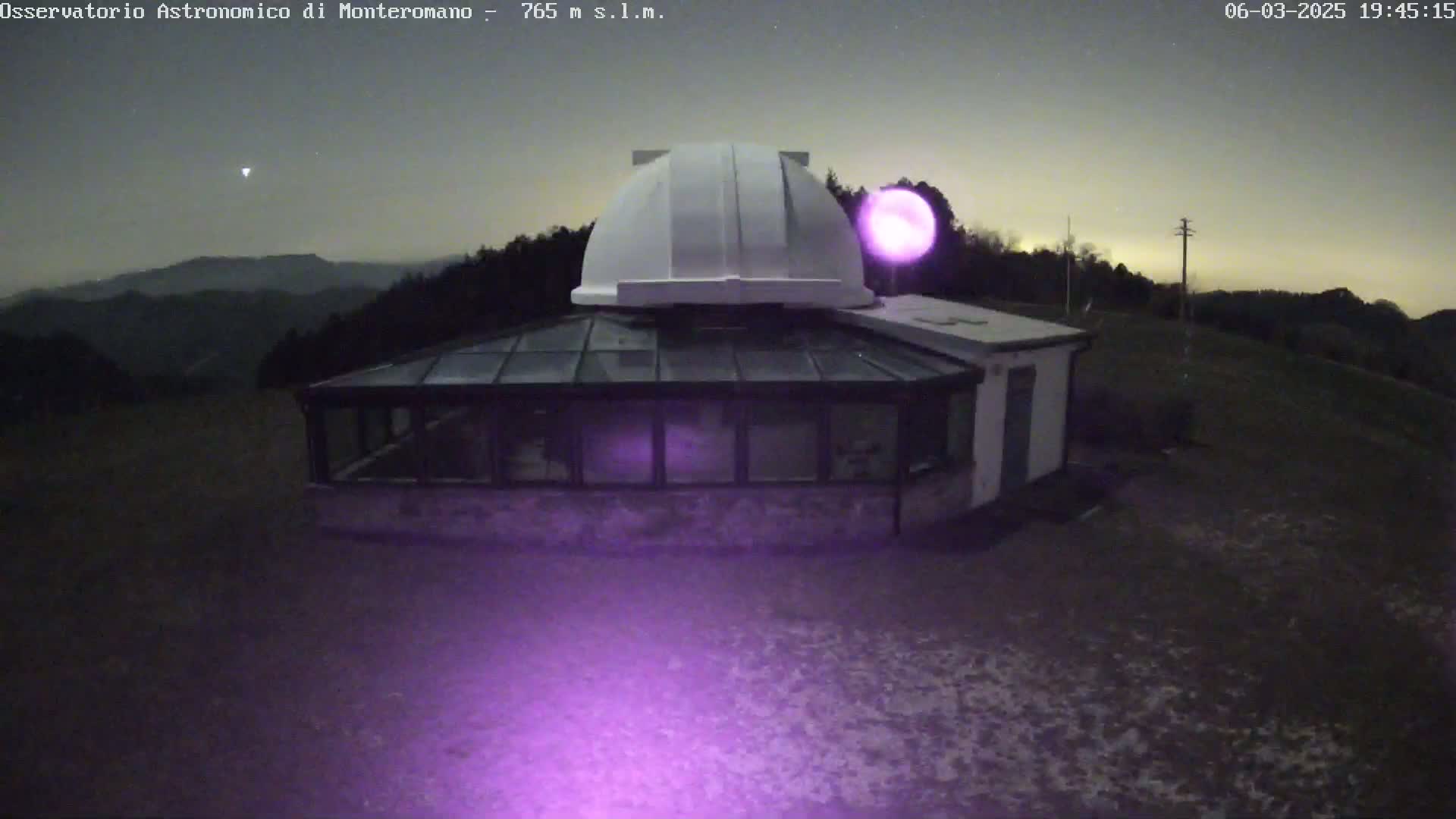 An astronomical observatory with a white dome and attached glass building sits on a hill under a twilight sky.