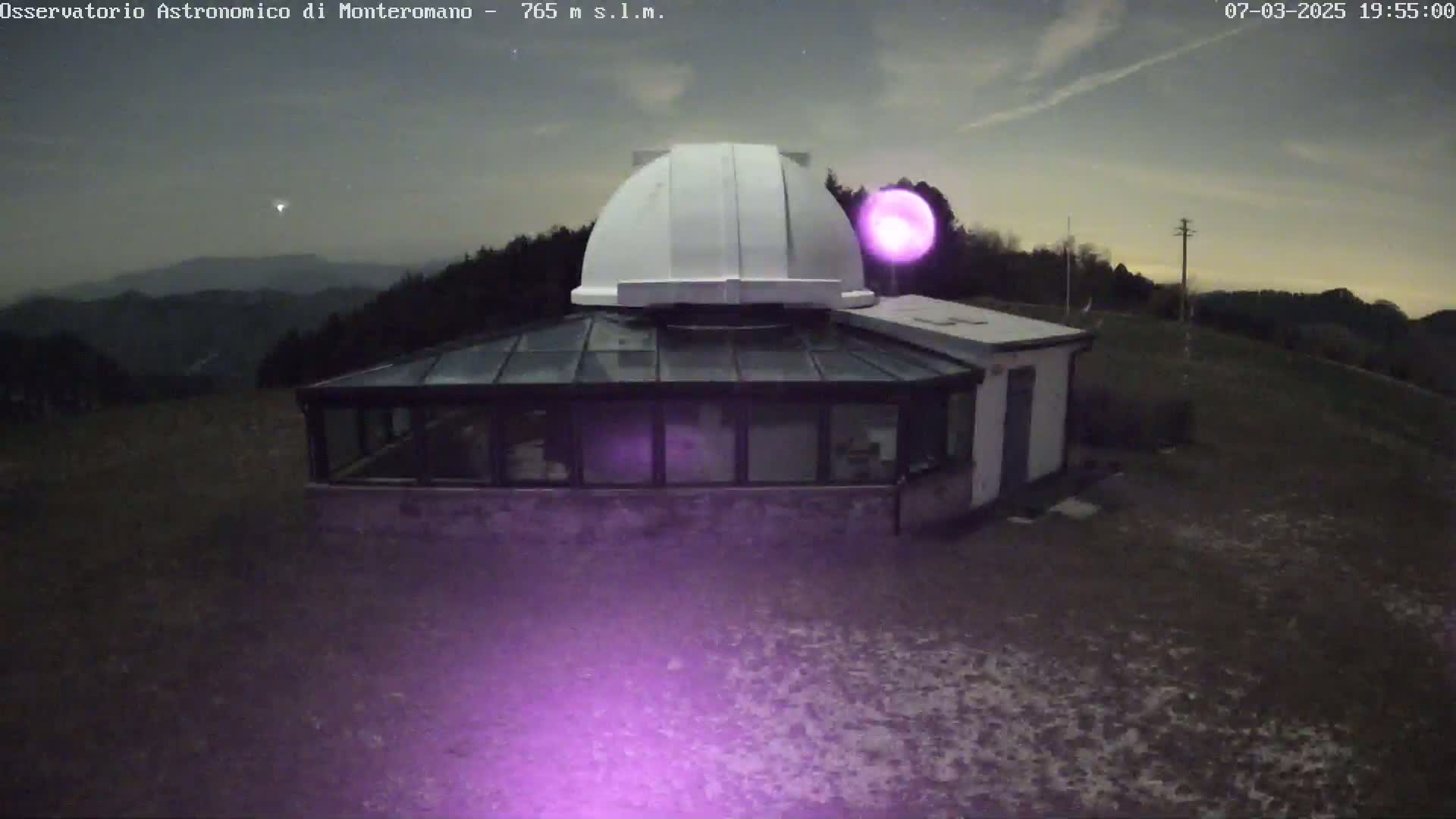 A white dome-shaped observatory building with an attached glass conservatory sits on a dark, slightly snowy ground under a mostly clear night sky.