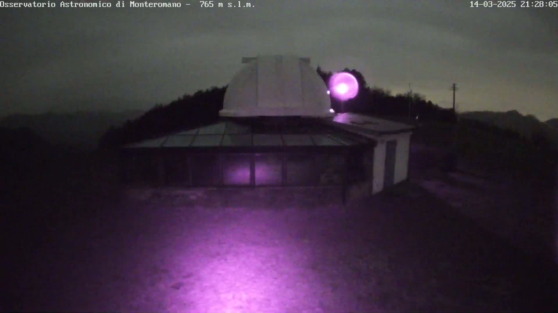 An observatory building with a dome is illuminated by a purple light at night under an overcast sky.