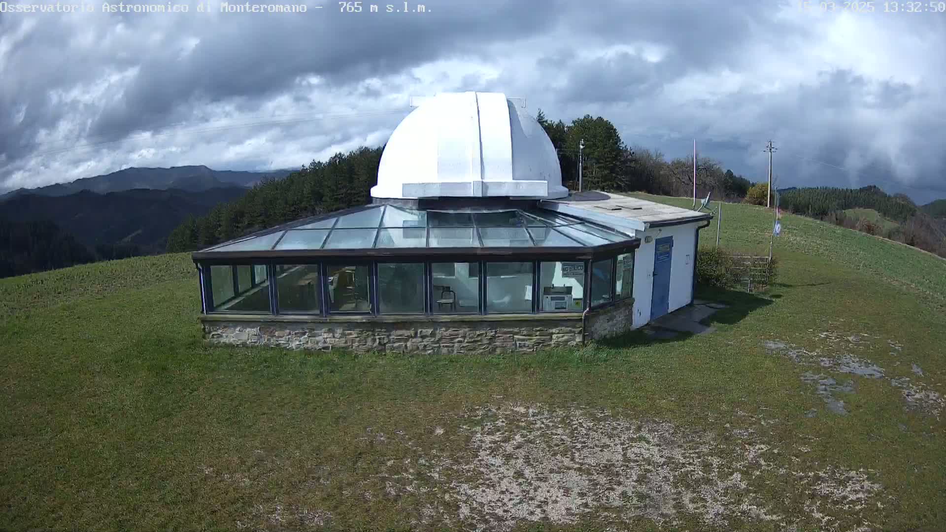 A white-domed observatory building with a glass sunroom sits atop a grassy hill under a partly cloudy sky.