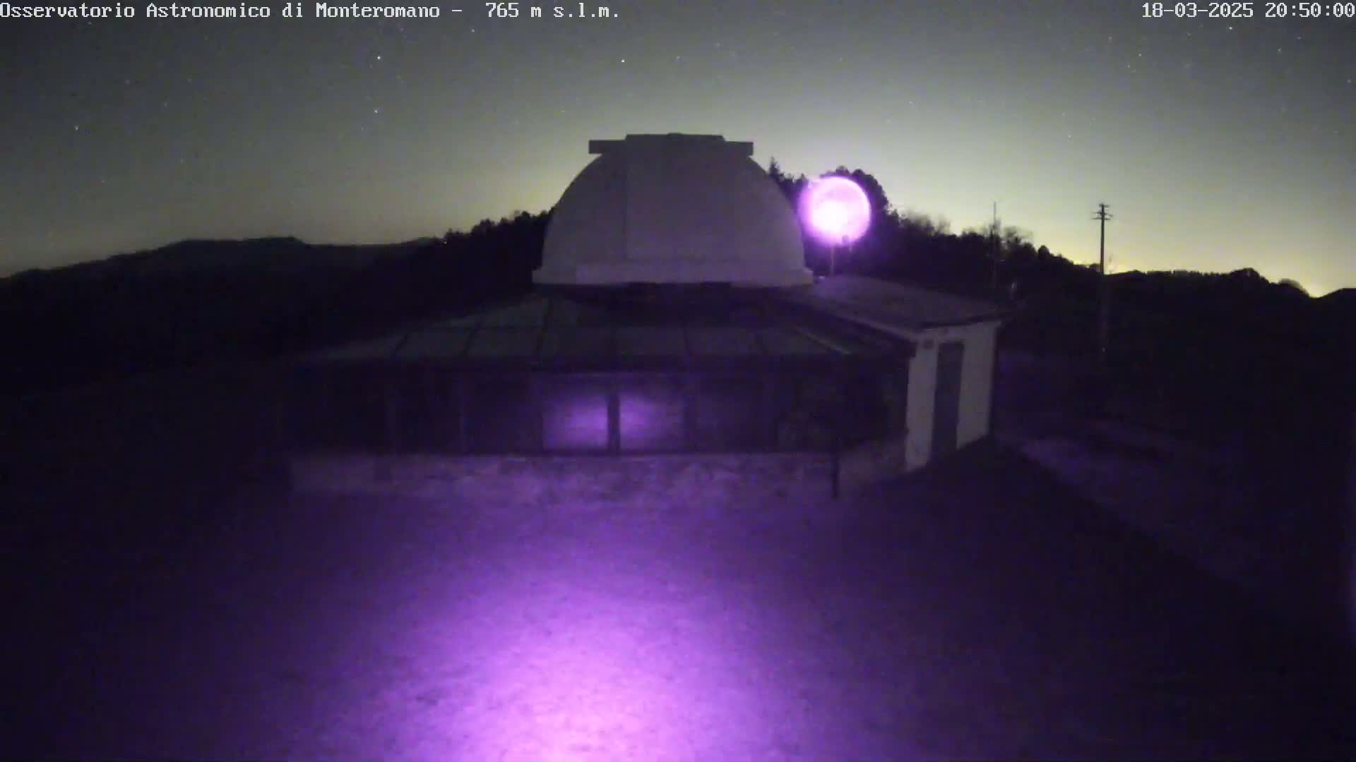 At night, under a starry sky, a low-light image shows an observatory building with a dome, illuminated by a purple light source.