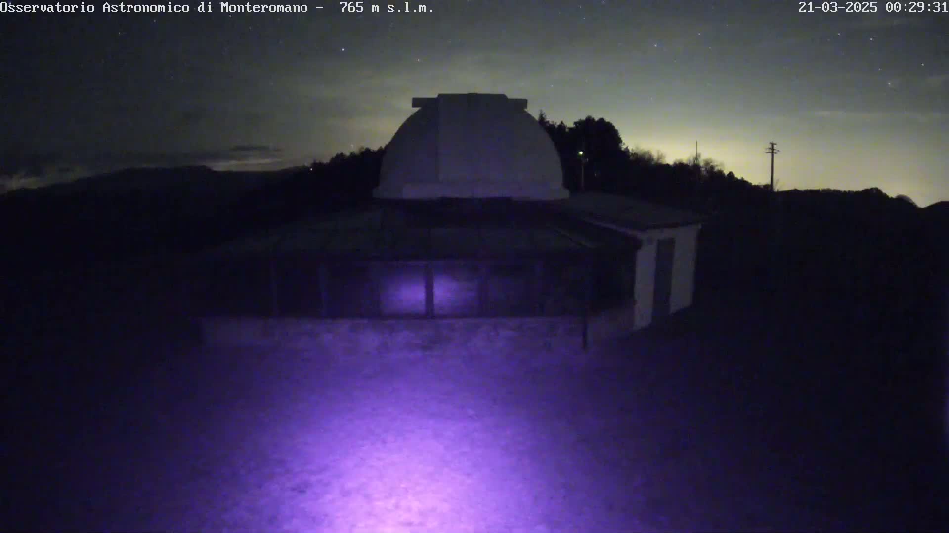 Under a mostly clear, starry night sky, a low-light image shows an observatory building with a dome on top.