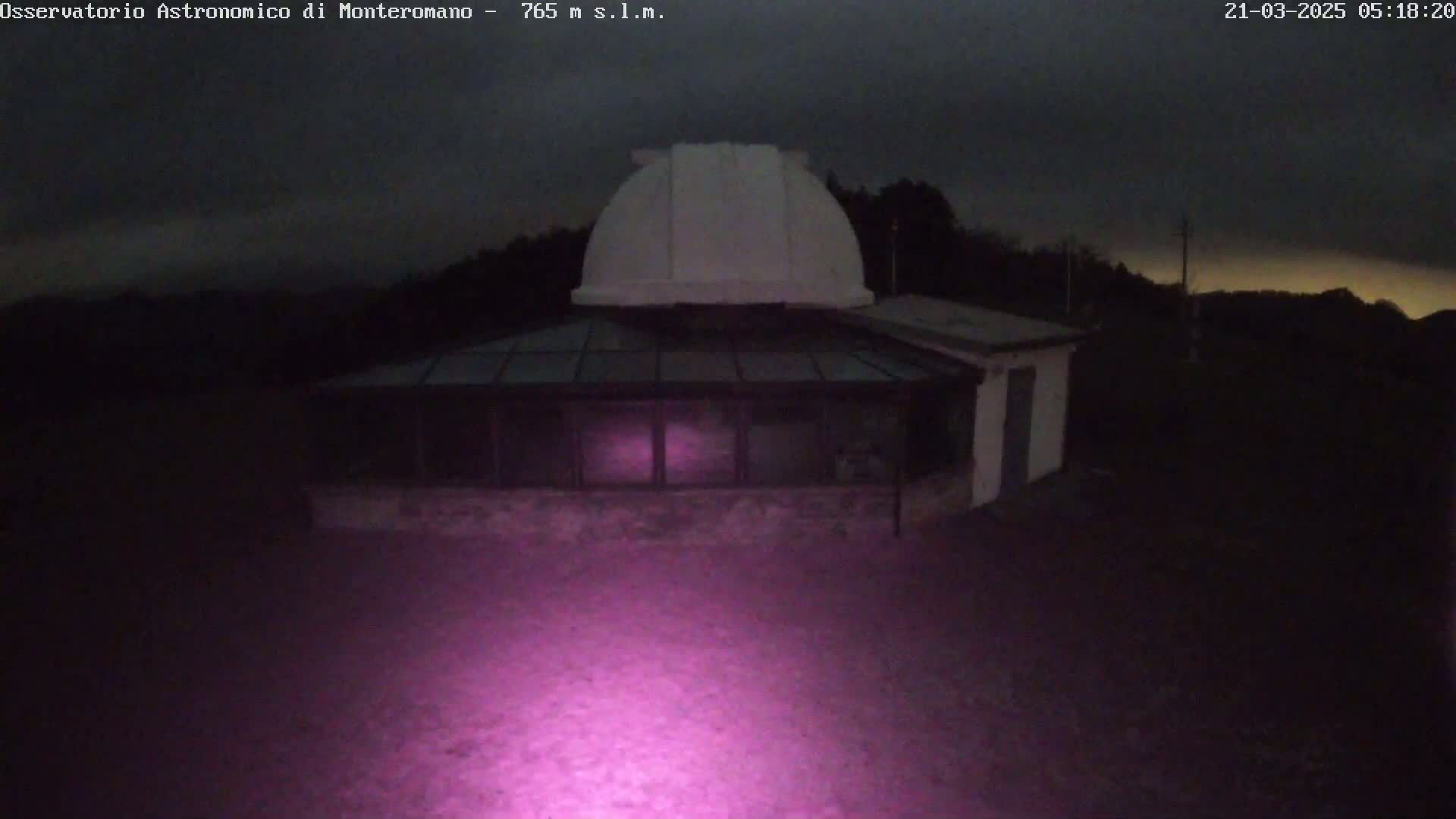 A low-light nighttime image shows an observatory building with a dome under a dark, cloudy sky.