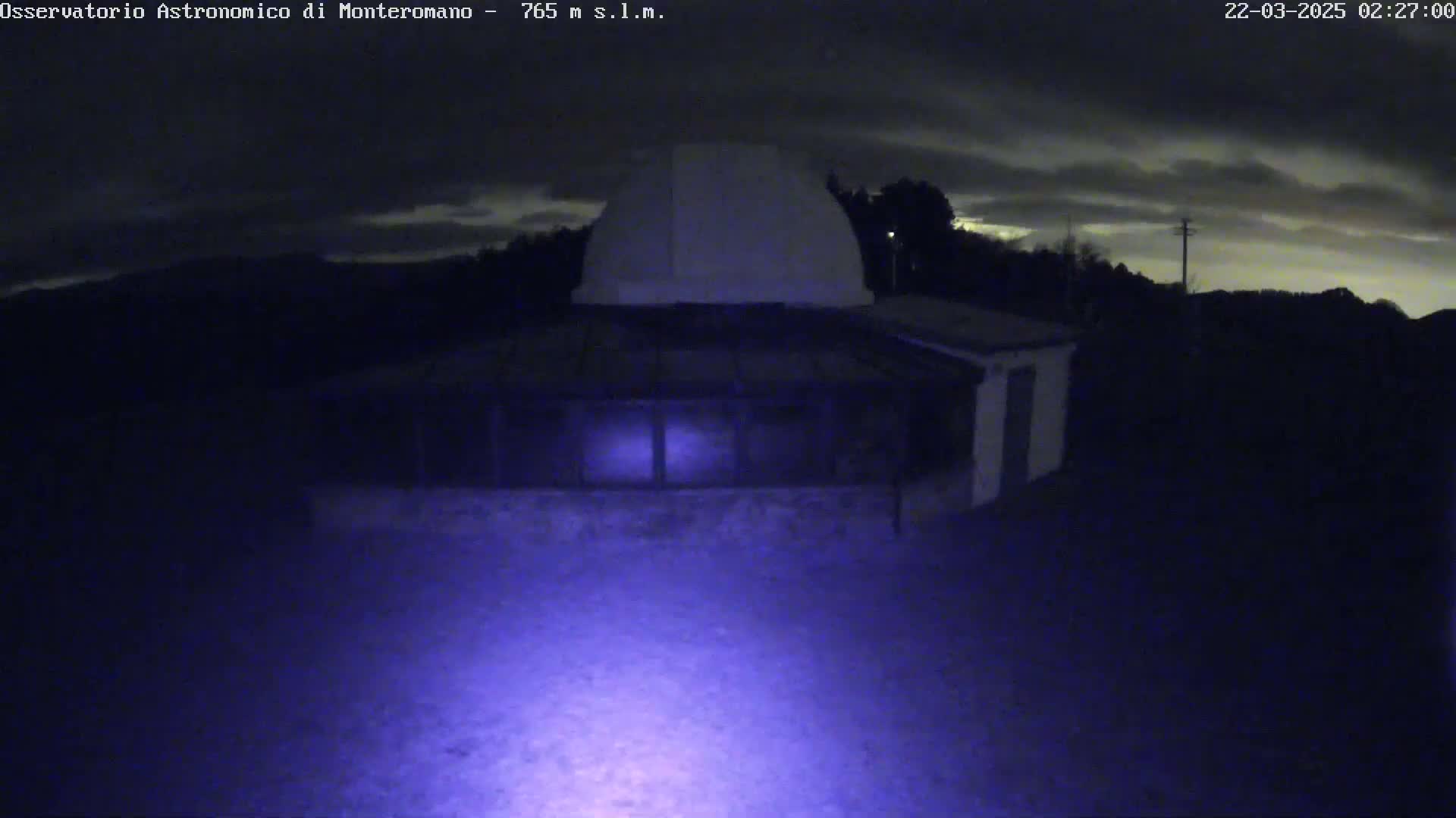 A low-light nighttime image shows an observatory building under a cloudy sky.