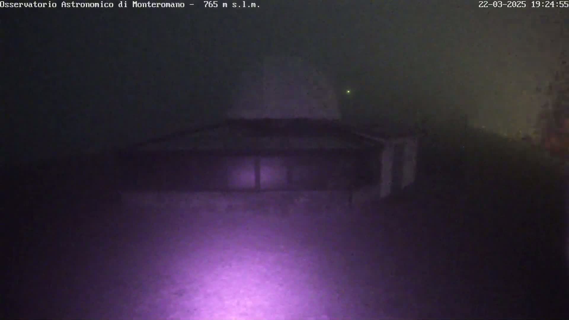 A low-light, nighttime image shows a building with a large, dome-like structure in hazy or foggy conditions.