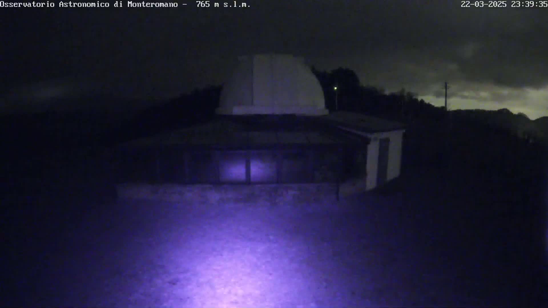 A low-light nighttime image shows a building with a dome on top, under a partly cloudy sky.