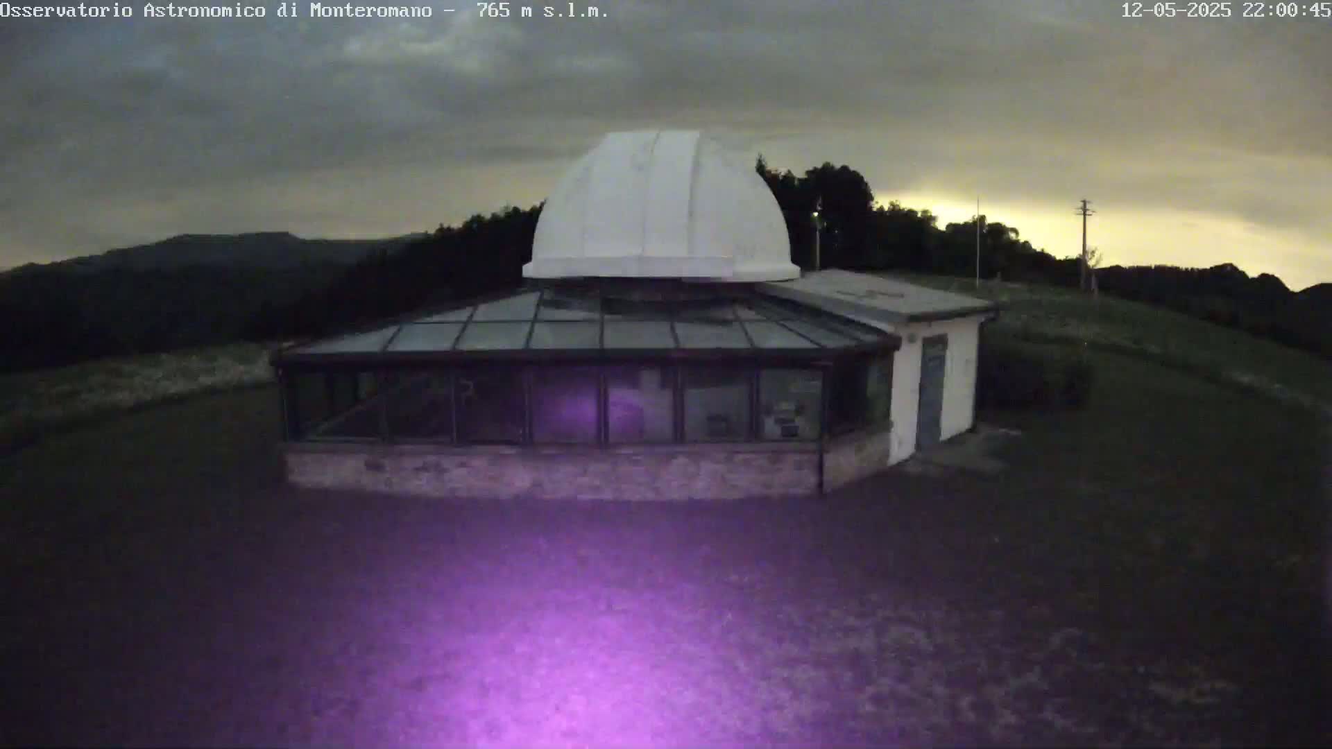 A white domed observatory building with a glass sunroom sits on a hilltop under a cloudy, twilight sky.