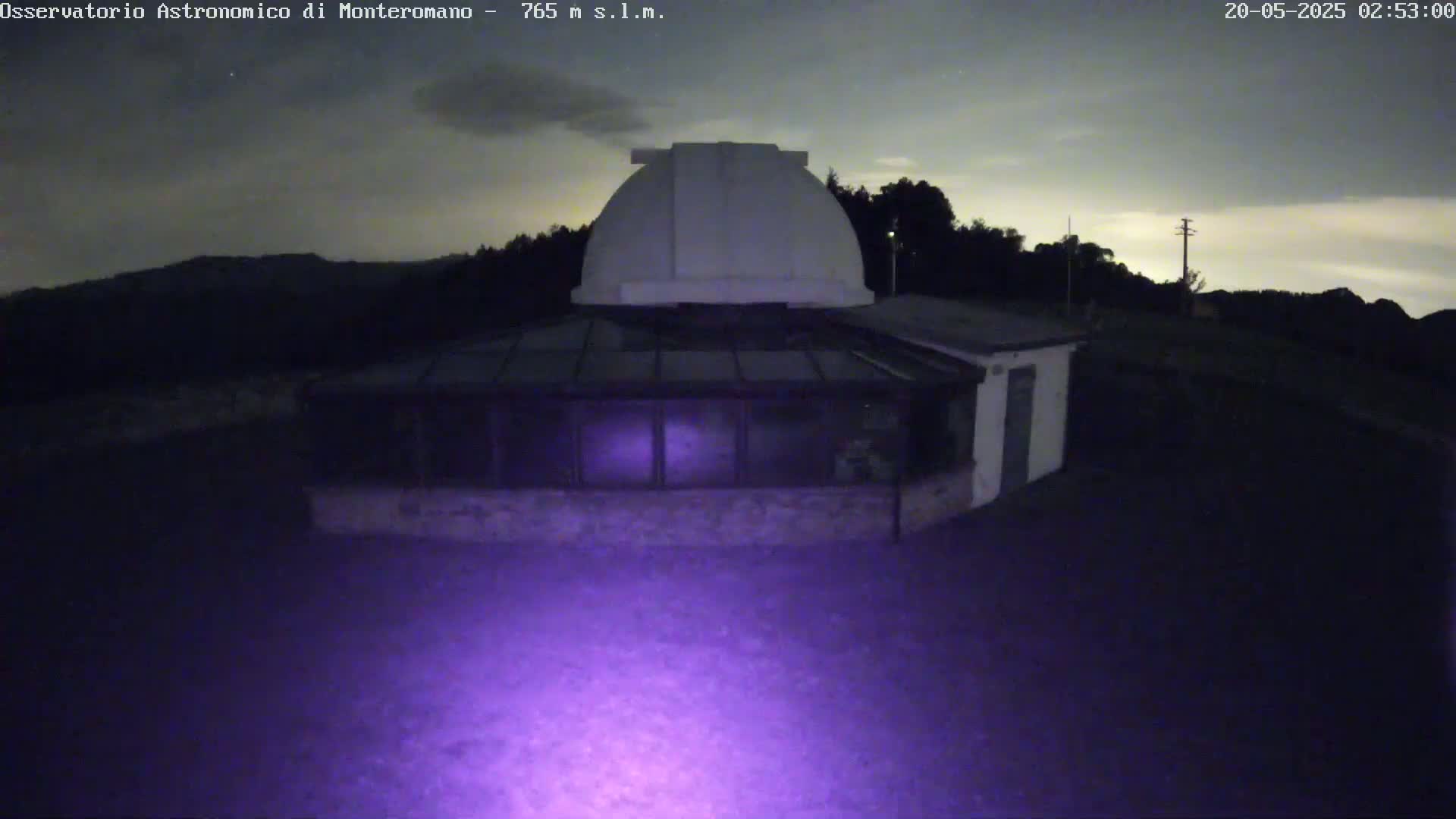 A white observatory dome with an attached glass-roofed building sits on a dark hillside under a mostly clear night sky.
