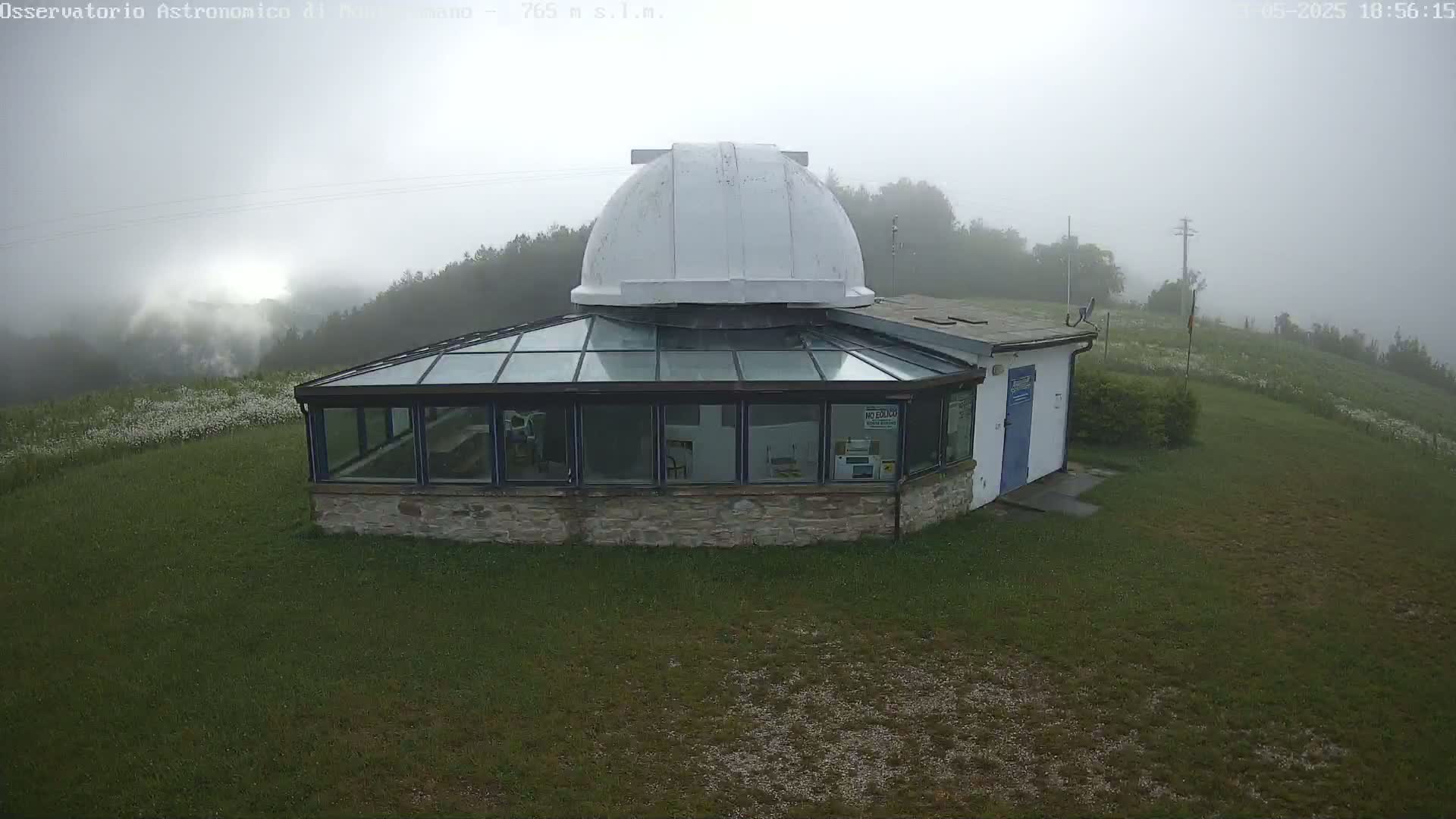 A stone building with a glass enclosure and a white dome sits on a grassy hill in foggy conditions.
