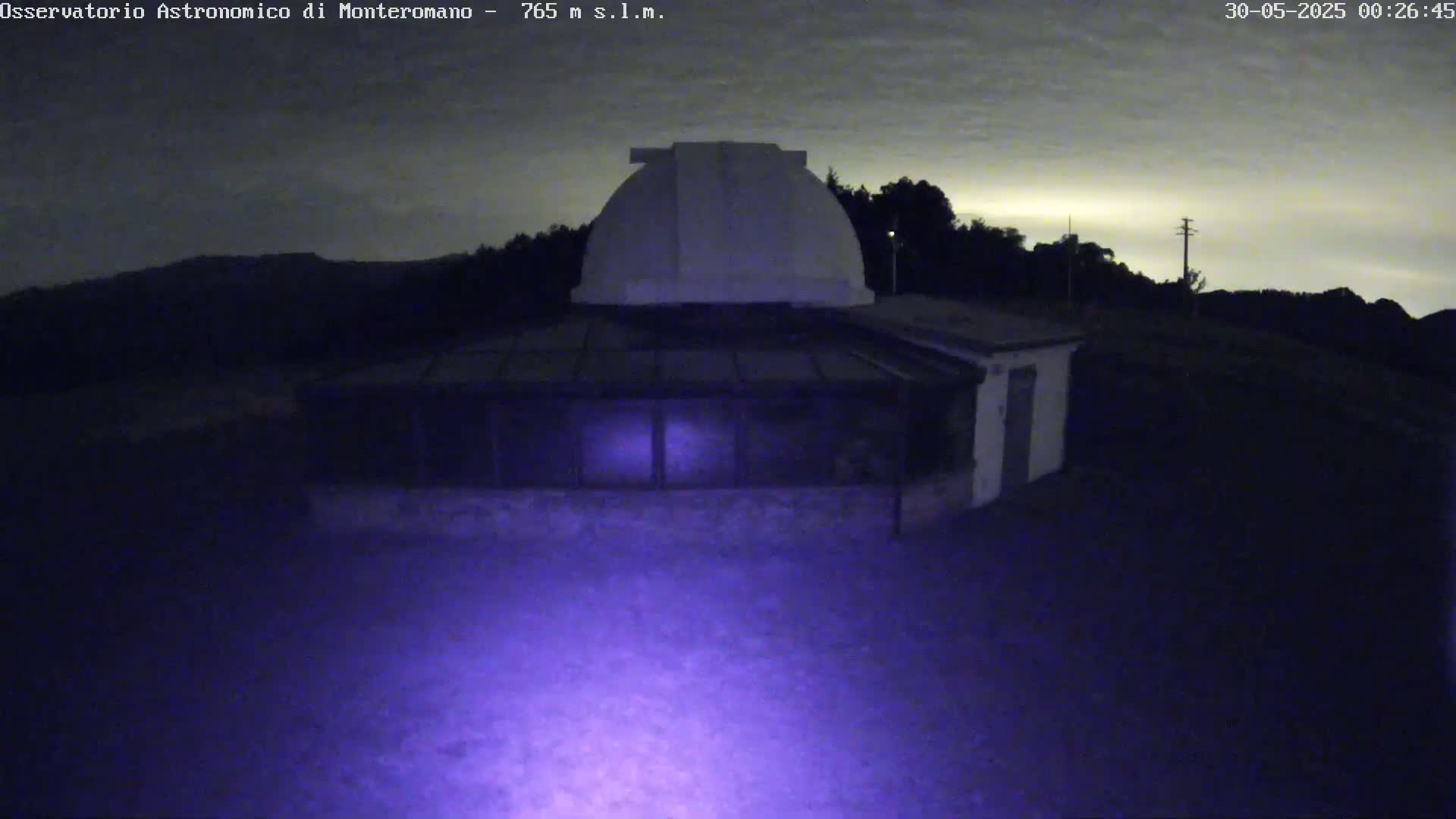 A nighttime image shows a low-light view of an observatory building with a dome under a mostly clear, dark sky.