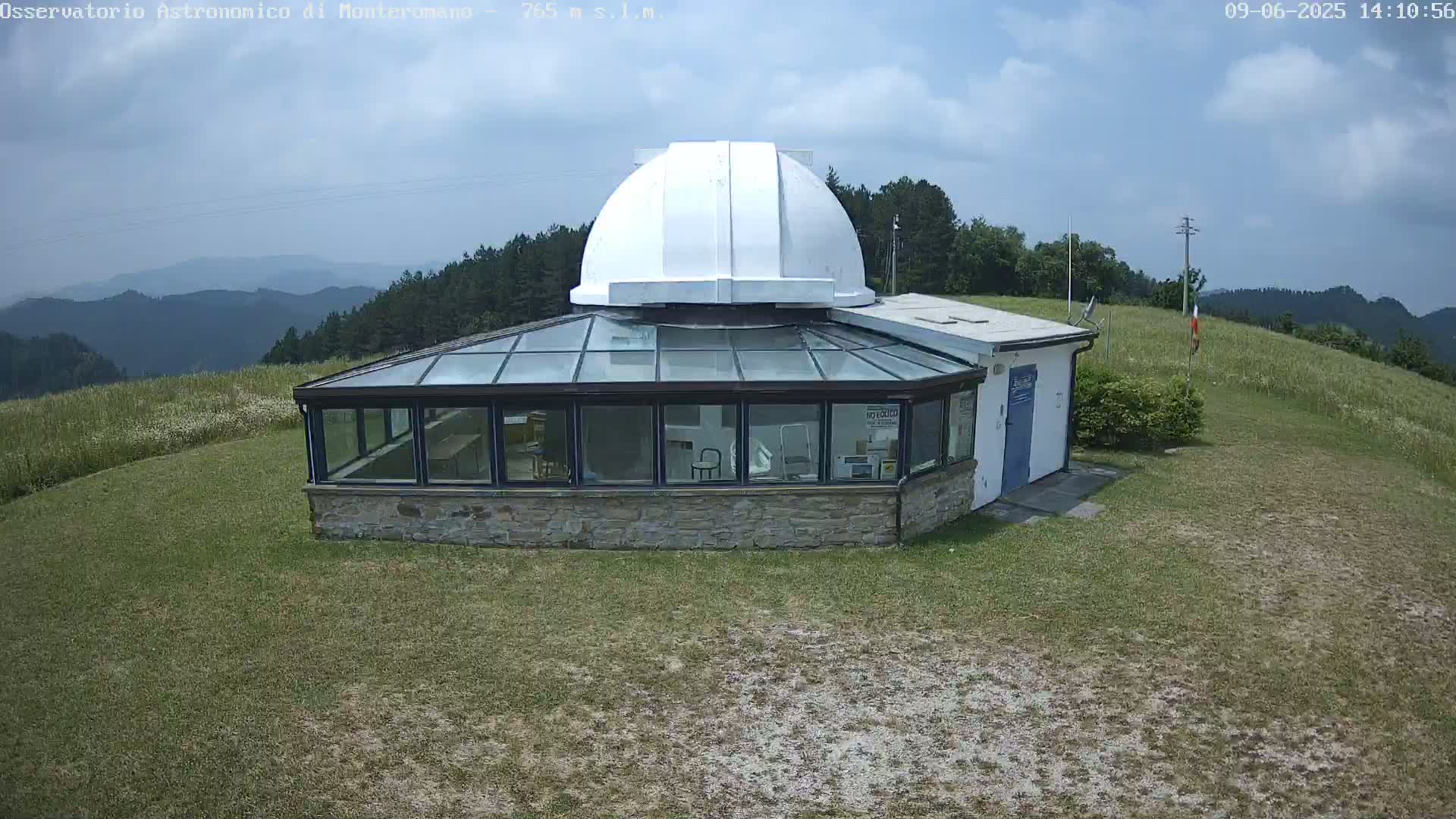 A stone building with a glass sunroom and a white dome sits on a grassy hilltop under a partly cloudy sky.