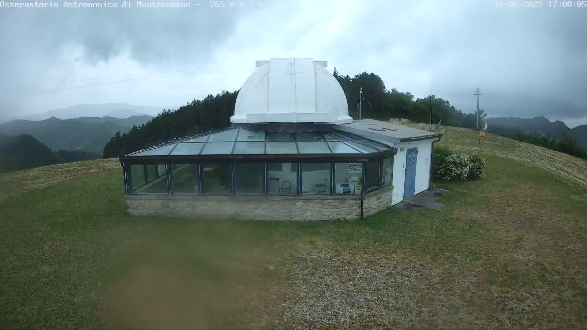 A white domed observatory building with a glass-roofed addition sits on a grassy hilltop under an overcast sky.