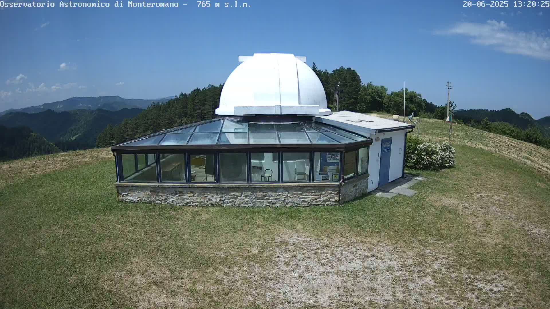 A stone building with a glass roof and a white dome sits atop a grassy hill under a clear blue sky.
