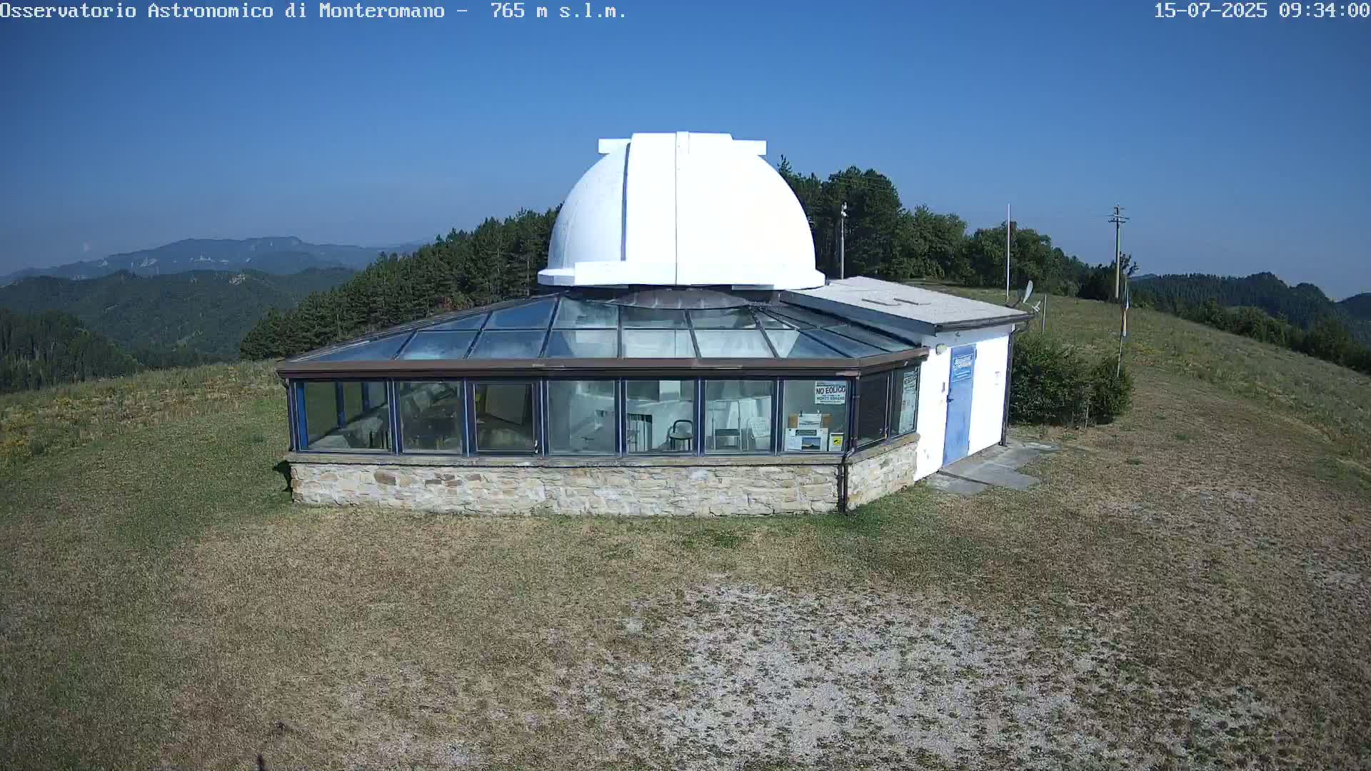 A stone building with a glass enclosure and a white dome sits on a grassy hilltop under a clear blue sky.
