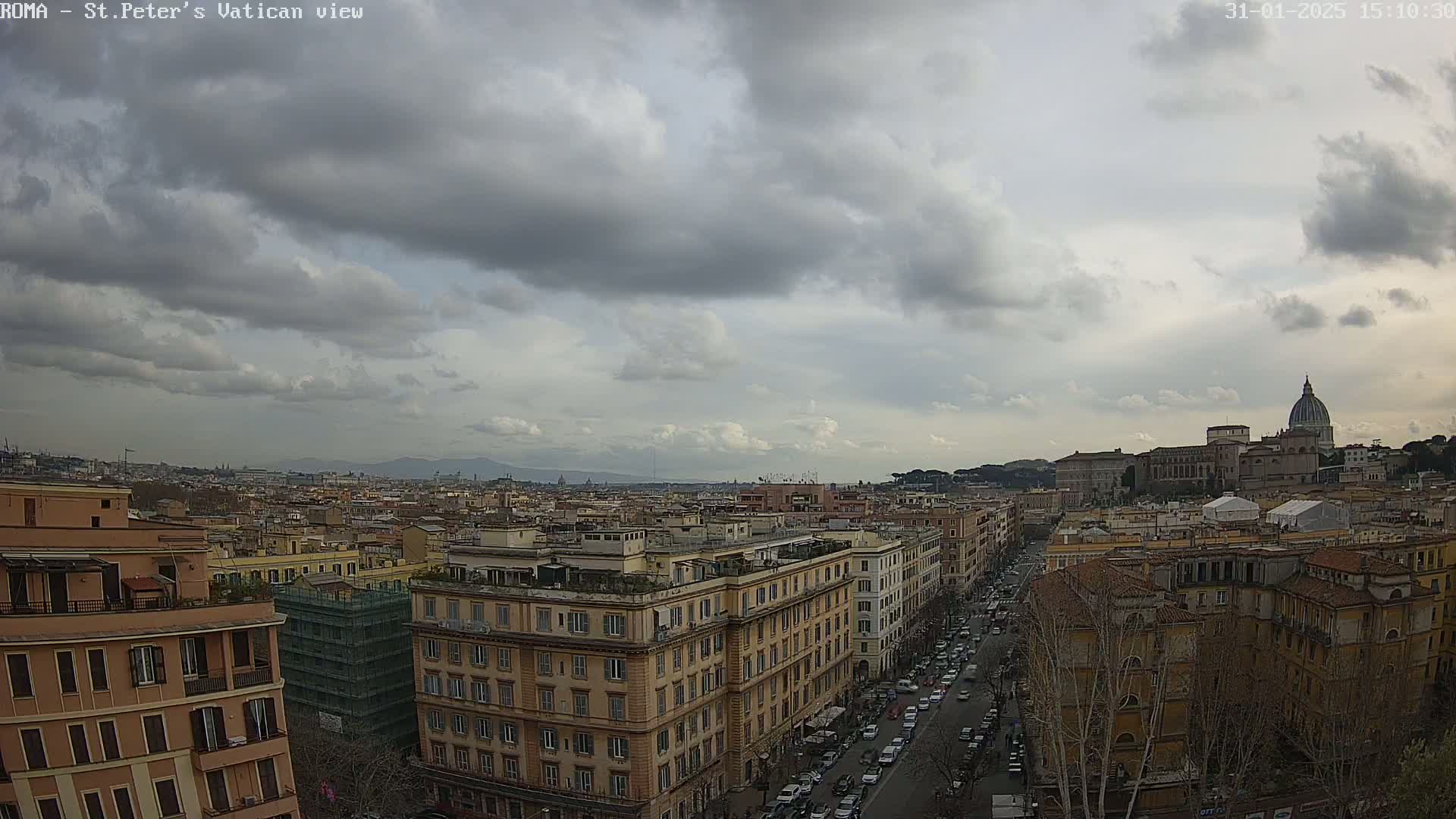 A high-angle view of a cityscape under a cloudy sky shows many buildings, including a large domed structure in the distance, and a street with cars below.