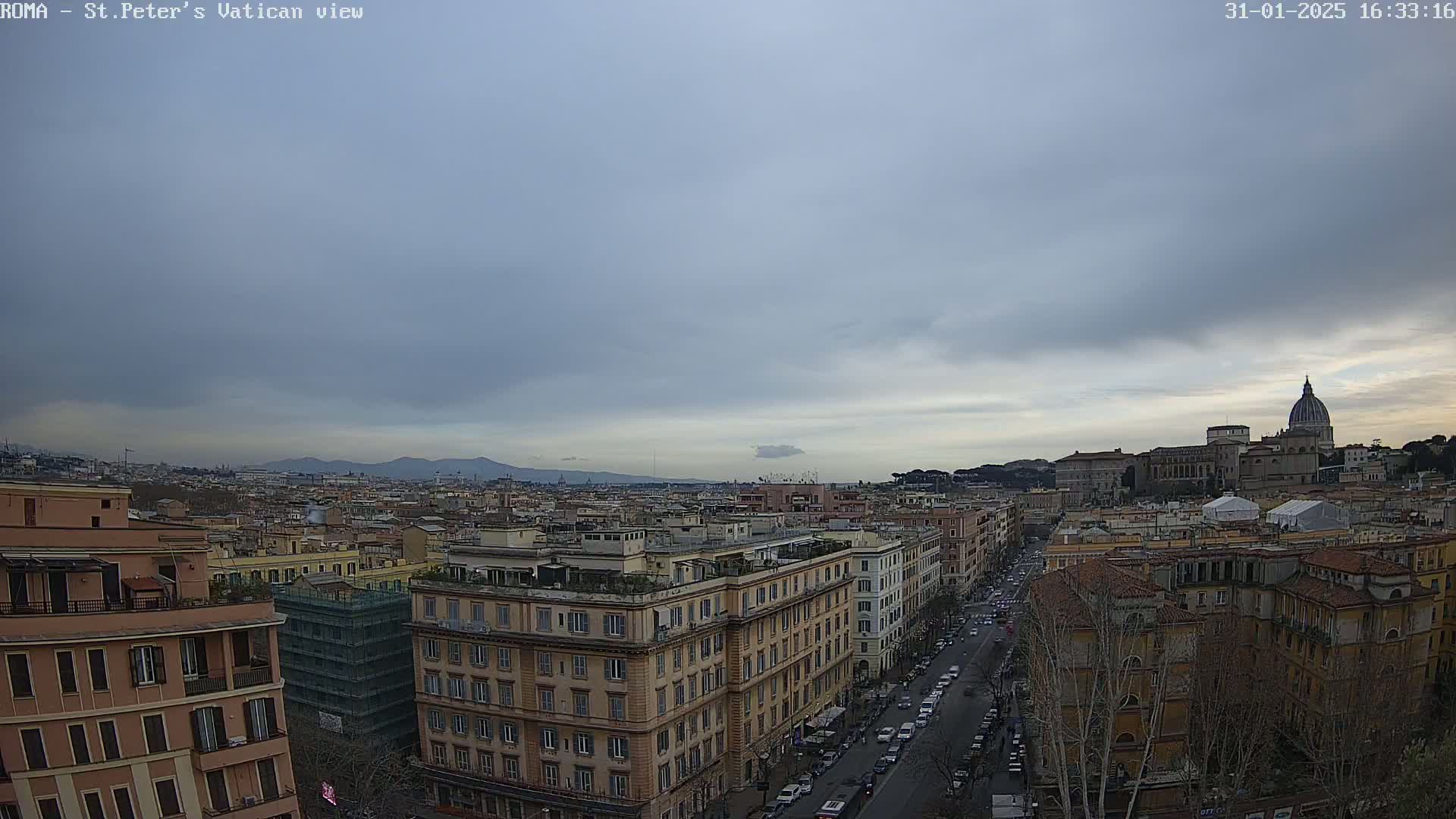 A high-angle view of Rome, Italy under an overcast sky, shows a cityscape stretching to the distant mountains, with St. Peter's Basilica visible in the background.