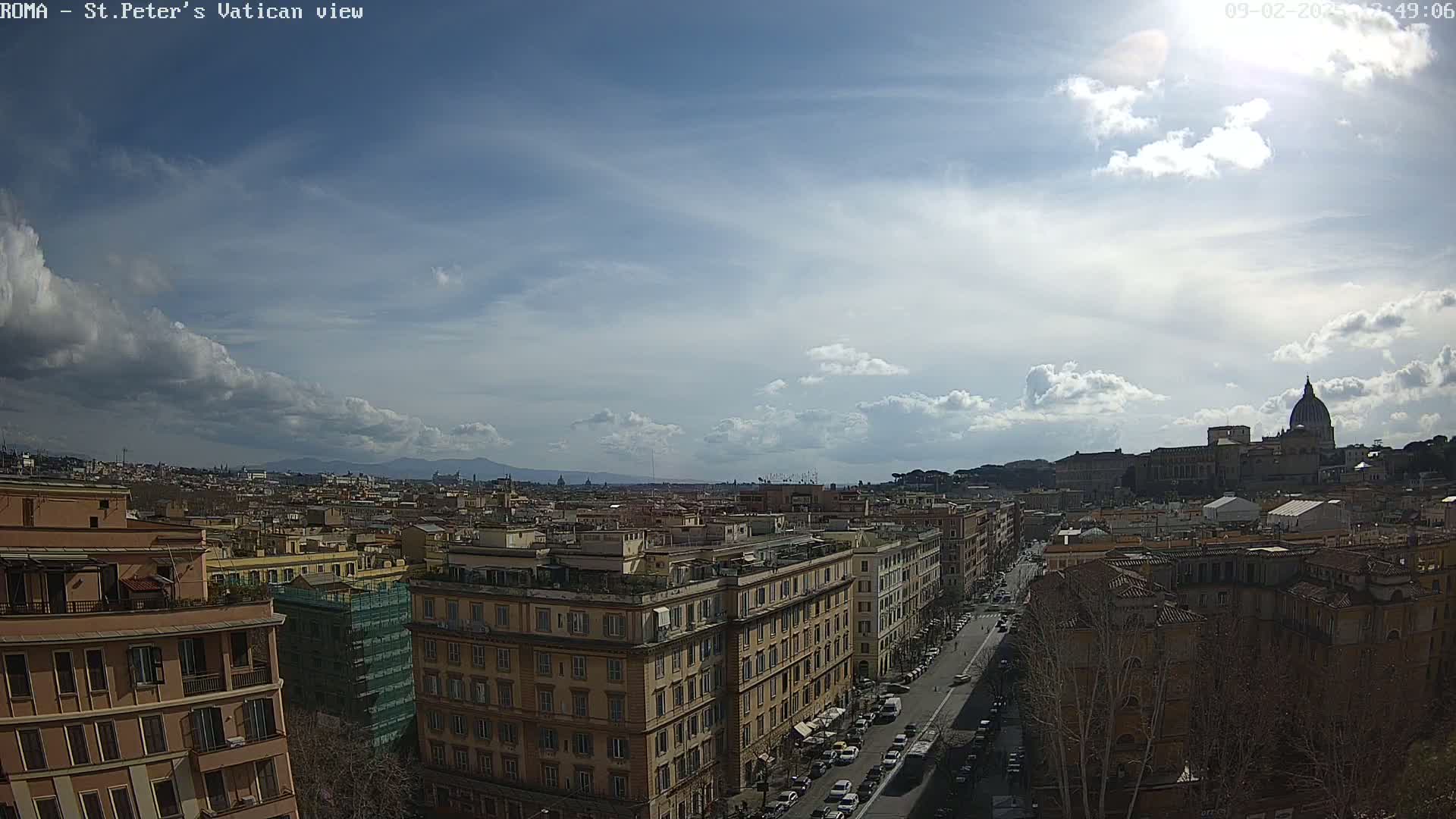 A partly cloudy sky overlooks a cityscape with a distant view of St. Peter's Basilica.