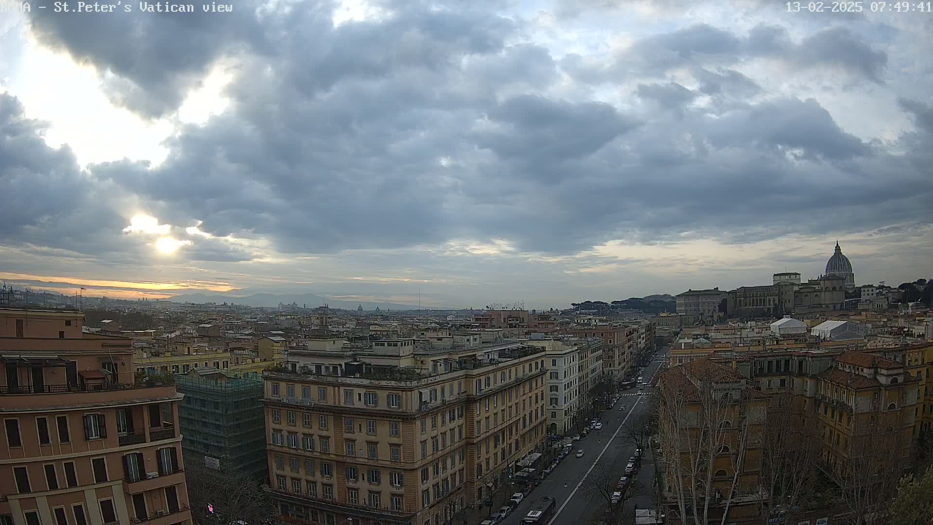 A partly cloudy sunrise over a cityscape, showing a distant view of St. Peter's Basilica.