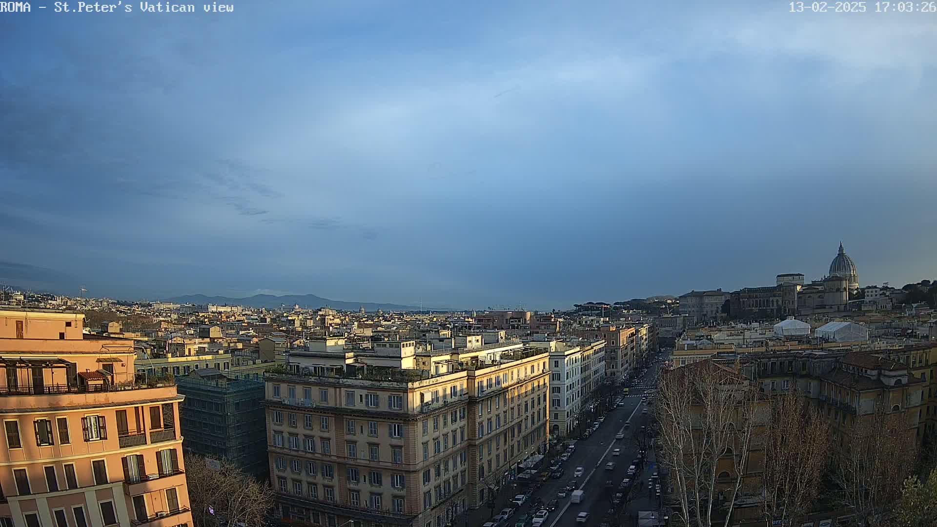 A panoramic view of Rome, Italy, under a mostly clear, dusky blue sky shows a cityscape with St. Peter's Basilica visible in the distance.