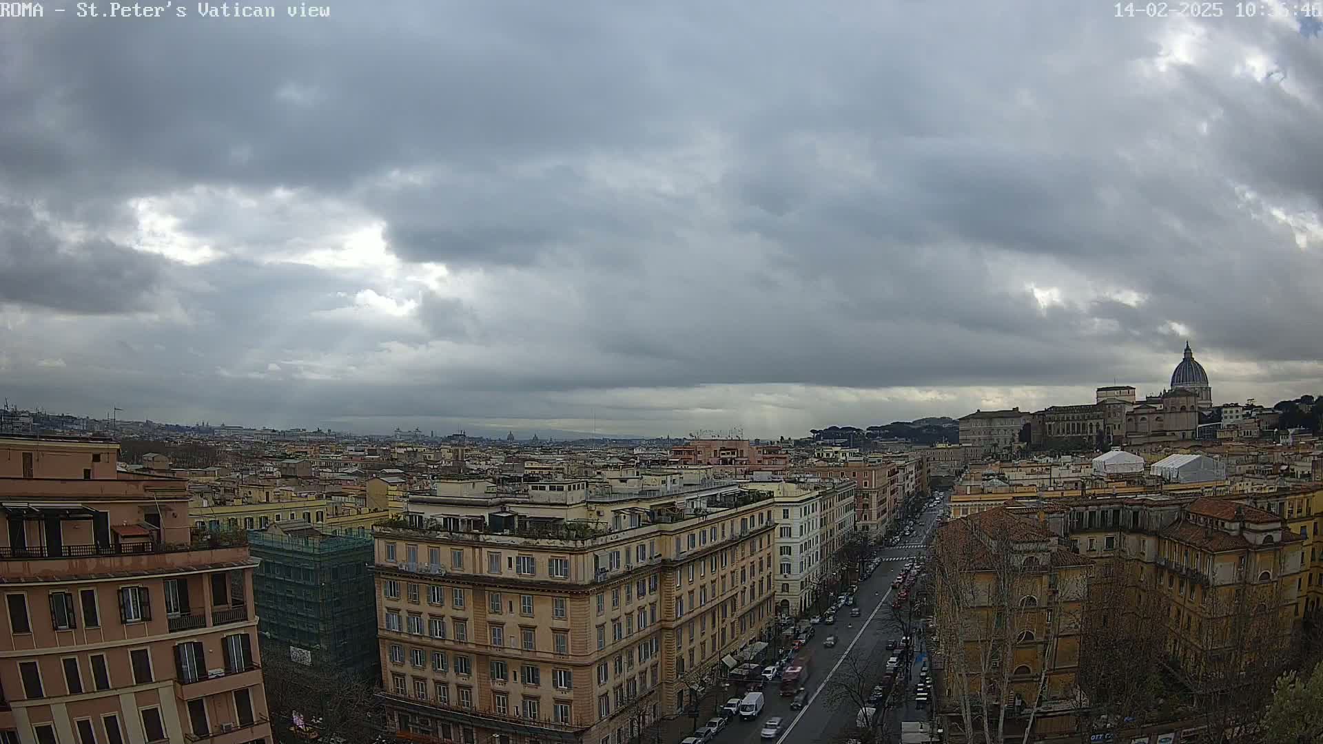 A panoramic view of a city under a cloudy sky shows buildings, streets with cars, and a large domed structure in the distance.