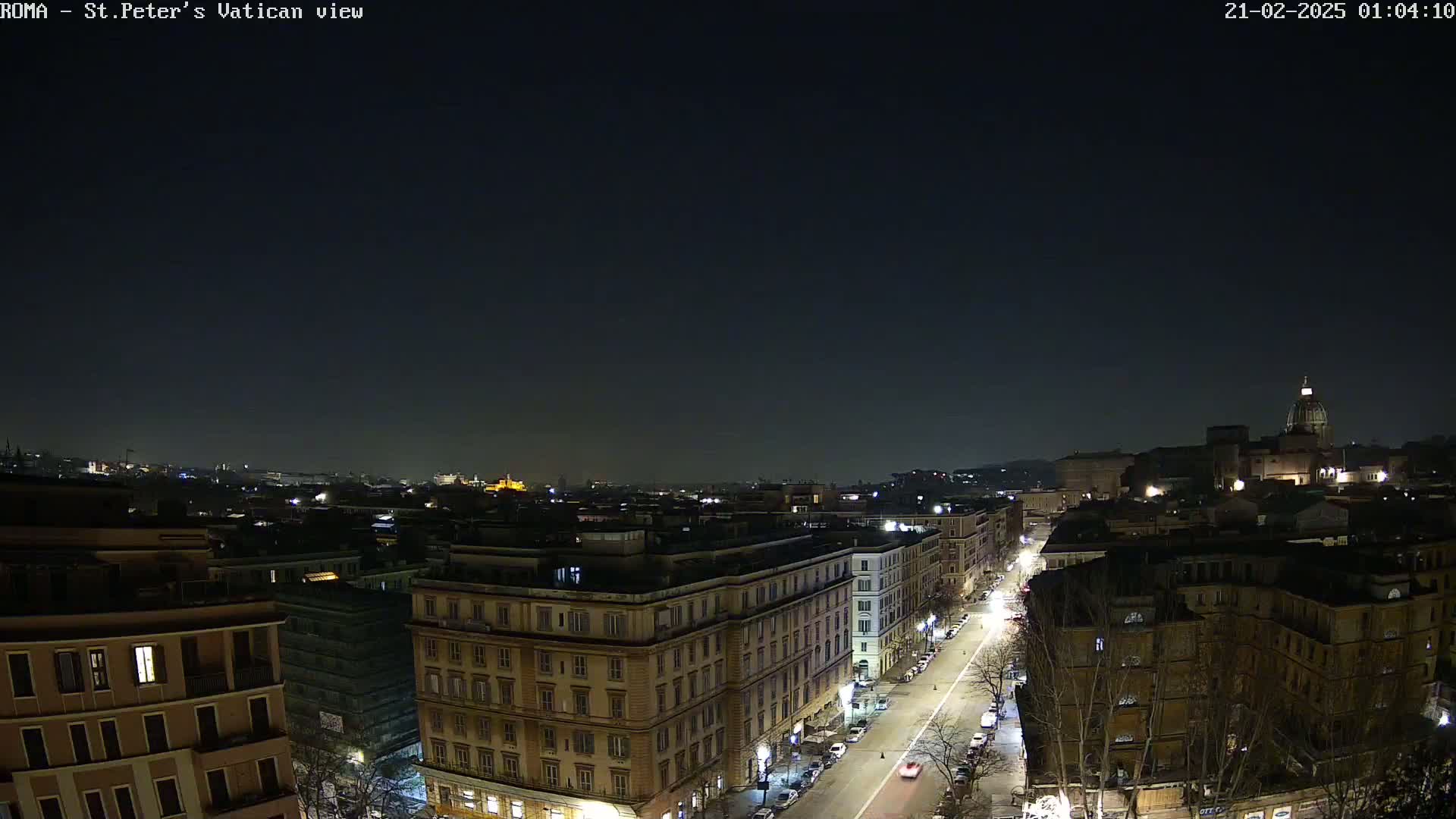 A nighttime, high-angle view of a city street scene, showing a portion of a city with buildings illuminated against a dark sky.