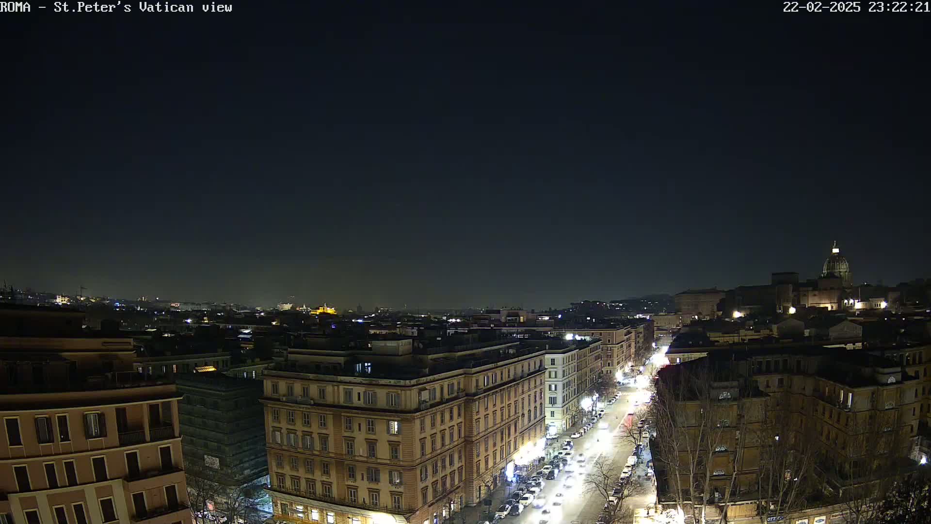 A nighttime view of a city, showing illuminated buildings and streets, with a dome-shaped structure visible in the distance under a clear, dark sky.