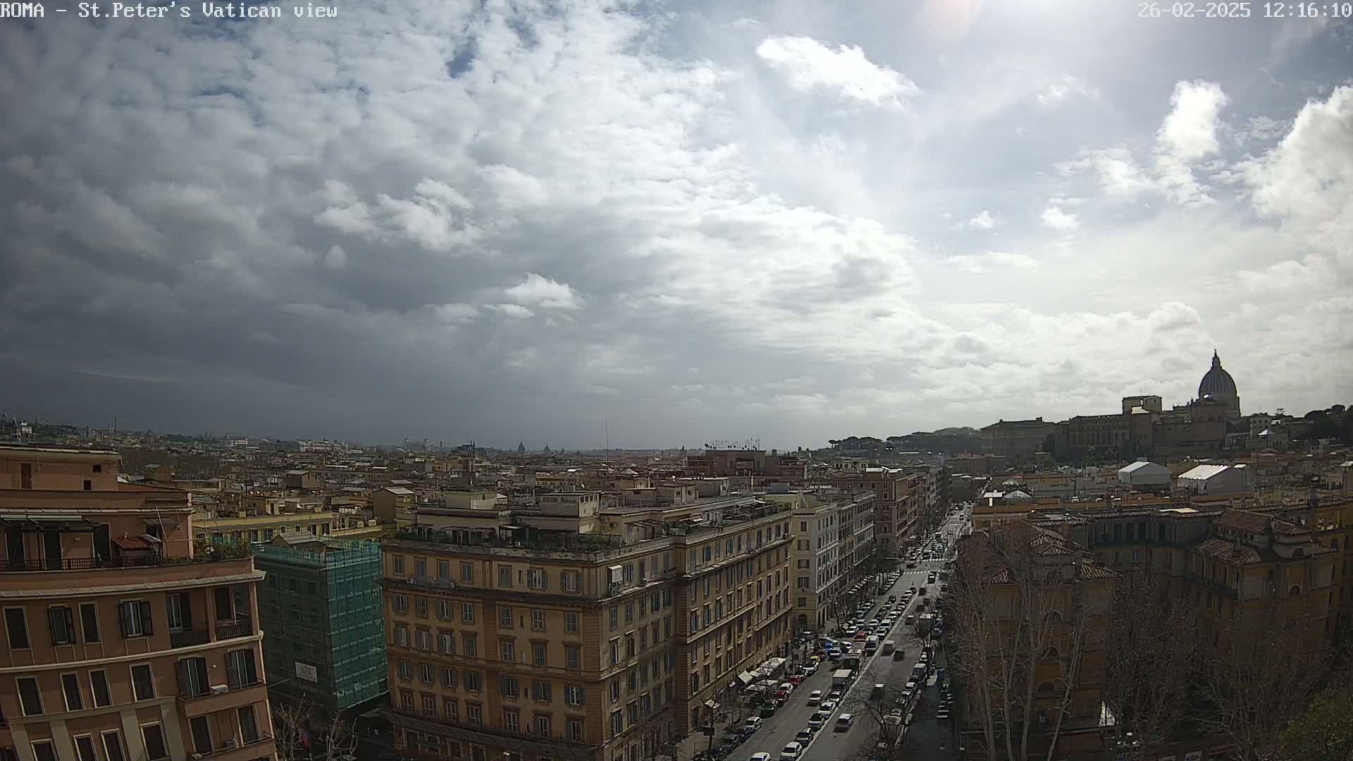 A partly cloudy sky overlooks a cityscape of Roman buildings and streets, with St. Peter's Basilica visible in the distance.