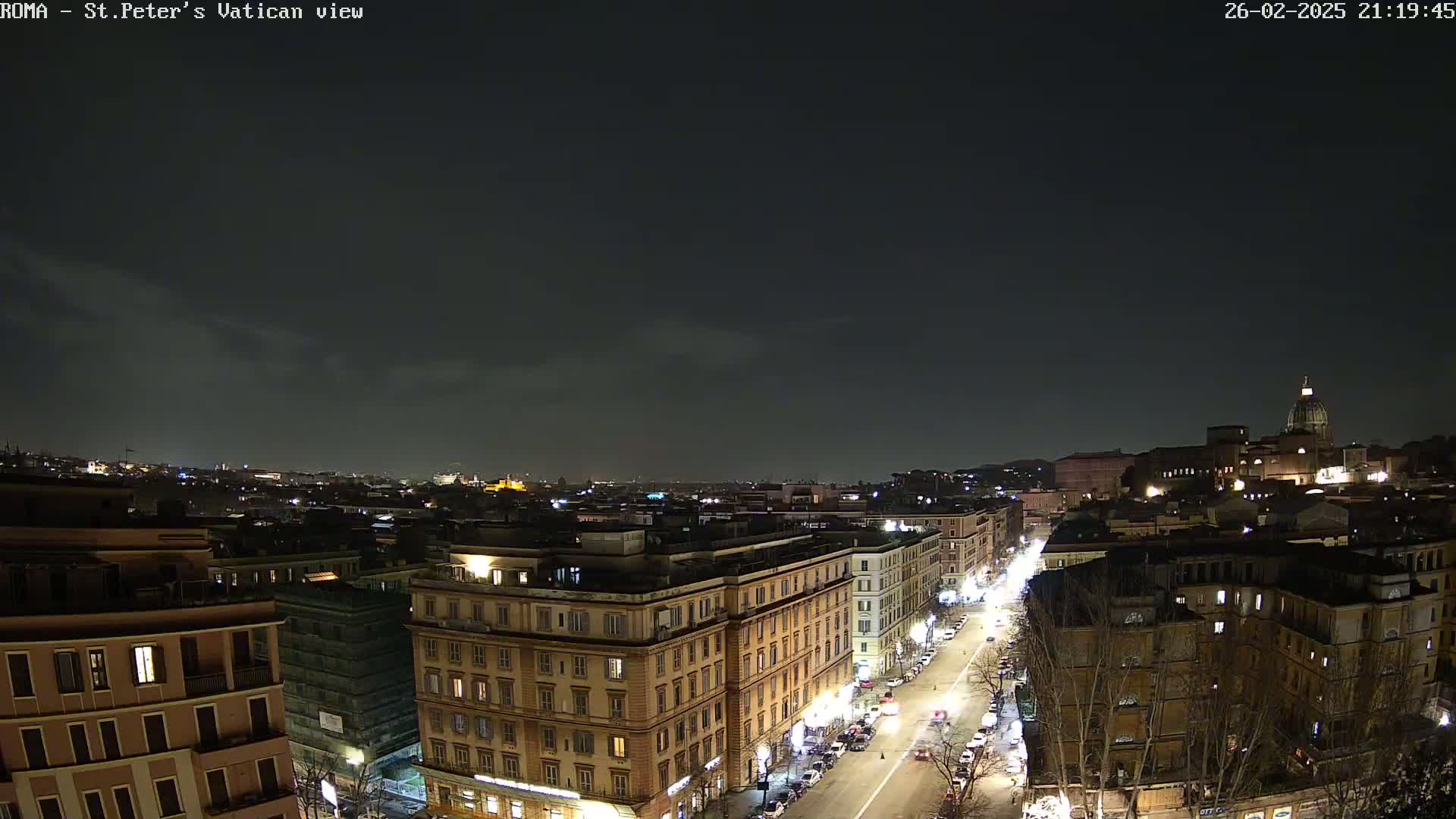 A nighttime aerial view of a city, showing illuminated buildings and streets under a mostly clear, dark sky.