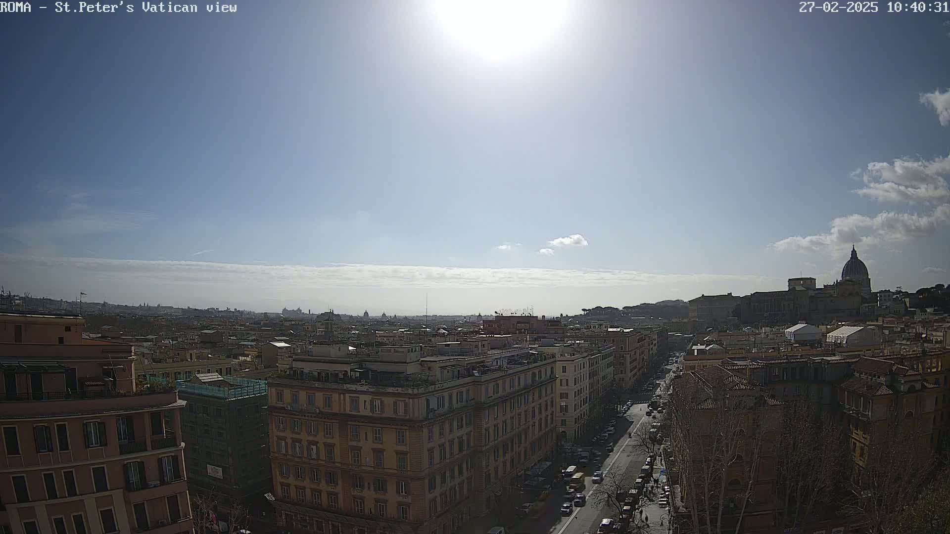 A sunny day reveals a panoramic view of Rome, showcasing a cityscape with buildings and the dome of St. Peter's Basilica in the distance.