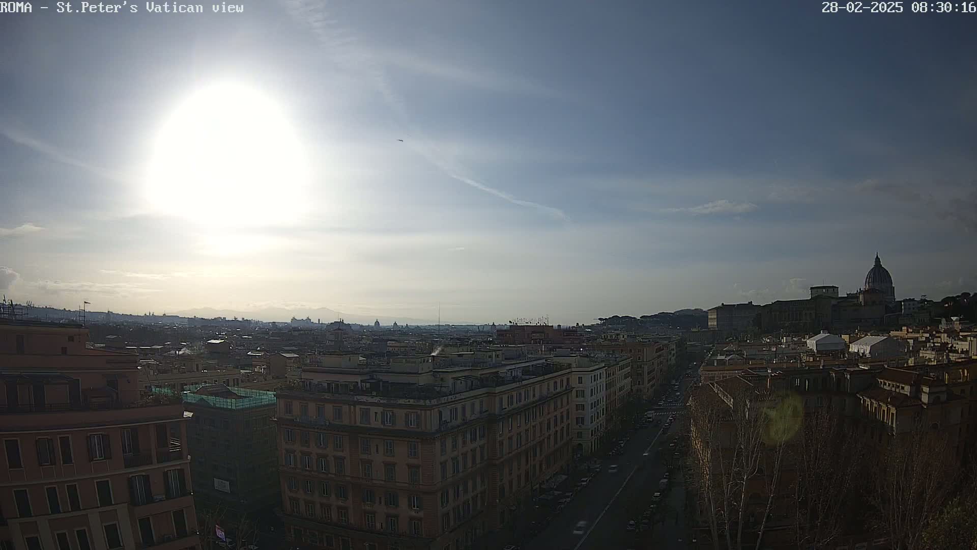 A bright, sunny day reveals a panoramic view of Rome, with the dome of St. Peter's Basilica prominent in the distance, overlooking a cityscape of buildings and streets.