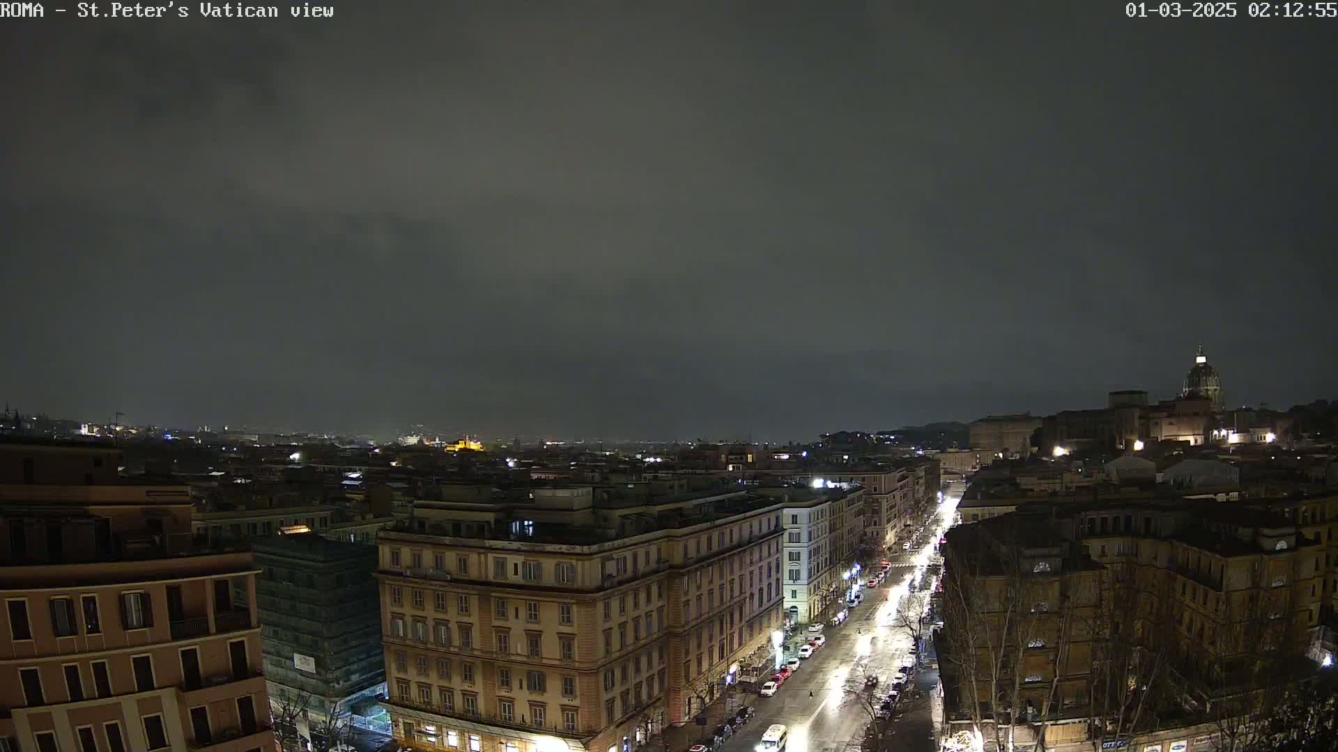 A nighttime view of a city street, lined with buildings, under a dark, cloudy sky.
