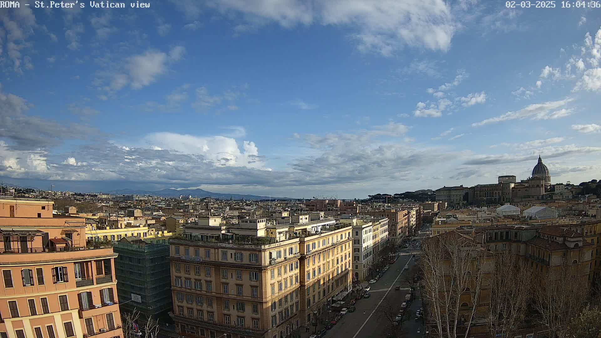 A partly cloudy sky overlooks a cityscape, with the dome of St. Peter's Basilica visible in the distance.