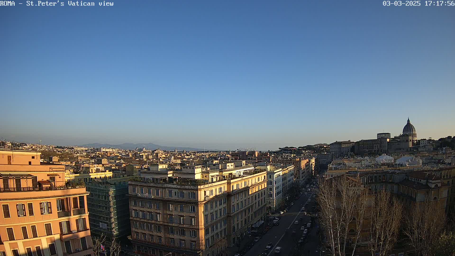 A clear, sunny view of Rome's cityscape, featuring St. Peter's Basilica in the distance and a street lined with buildings in the foreground.