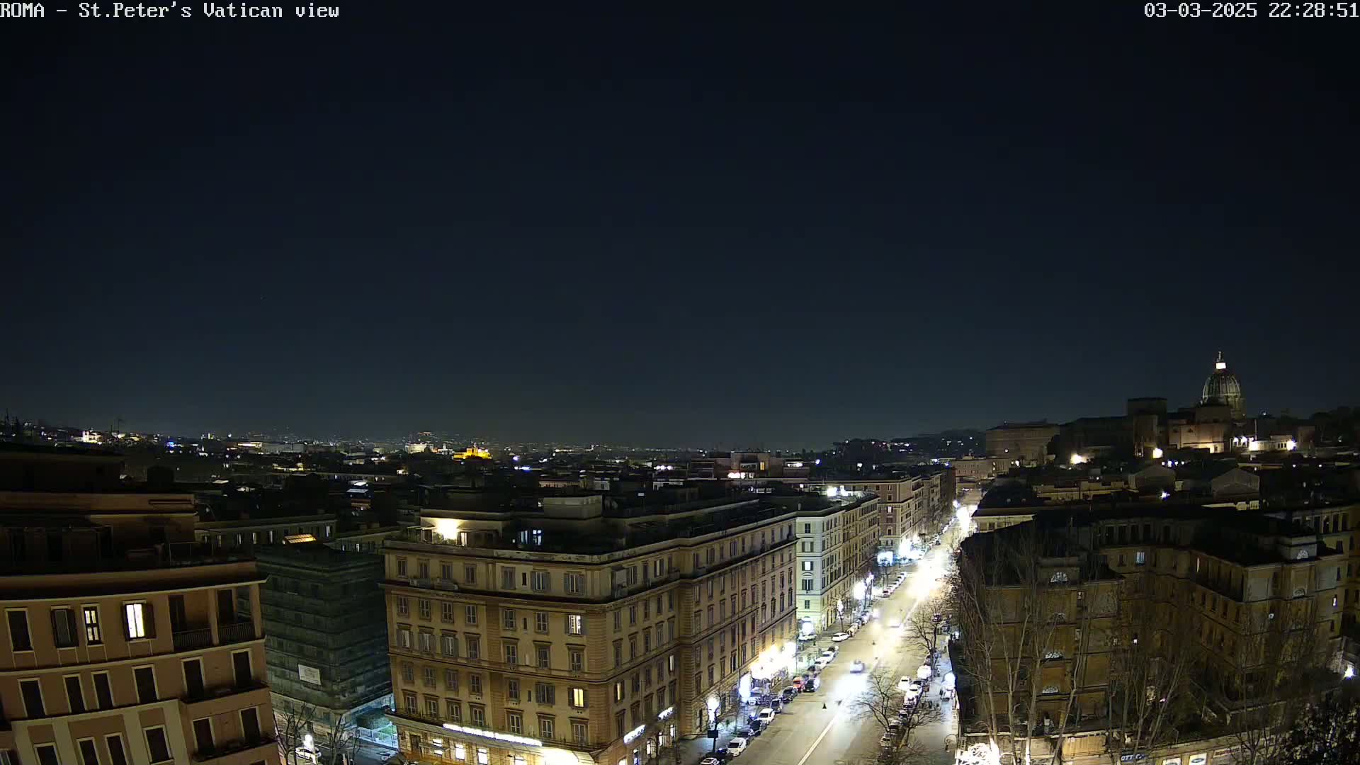 A nighttime, aerial view of a city, showing illuminated streets and buildings, with a clear, dark sky.