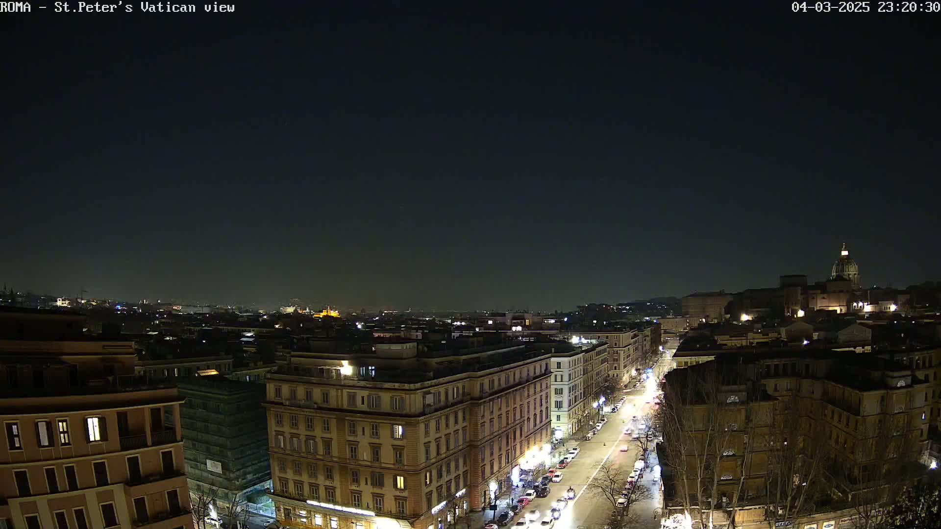 A nighttime, aerial view of a city street with buildings lit up, under a clear, dark sky.