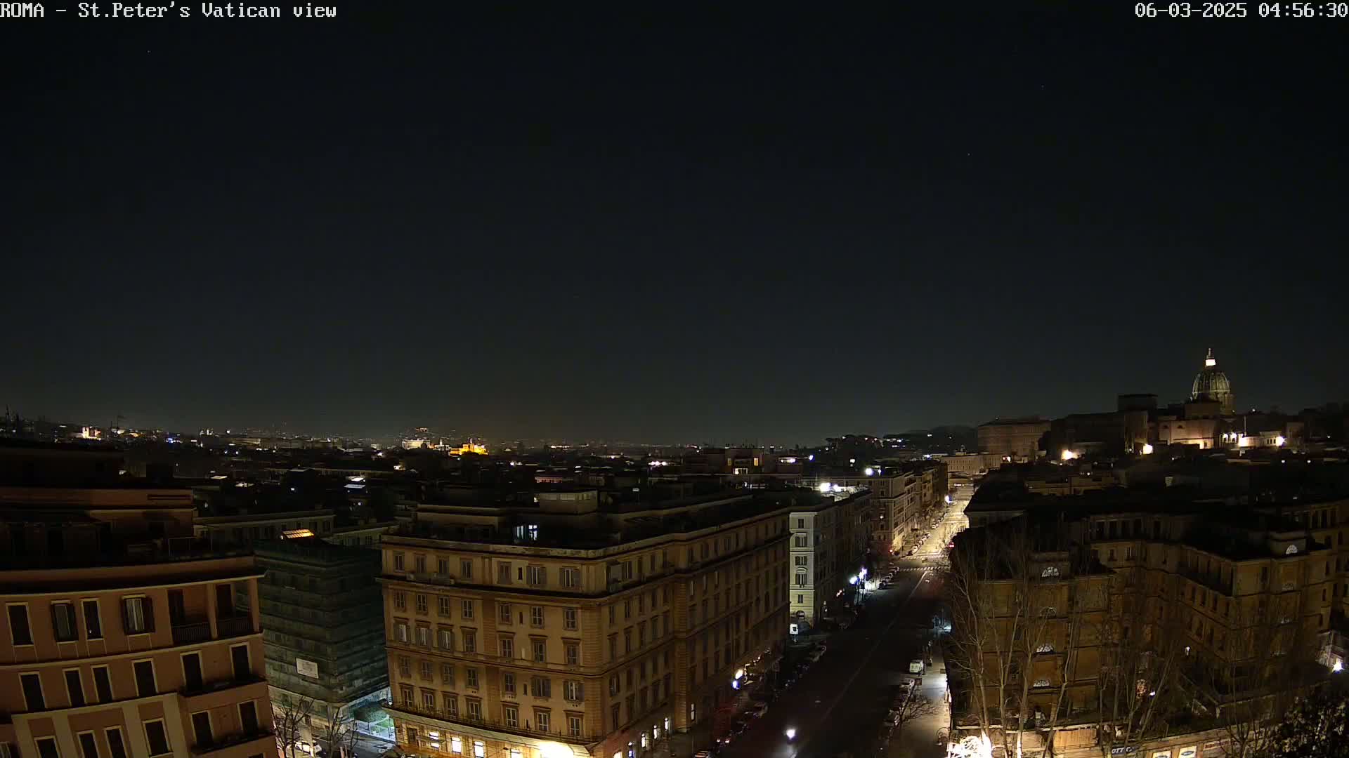 A nighttime, clear-skied view of a cityscape, featuring buildings illuminated by streetlights and a distant dome-shaped structure.