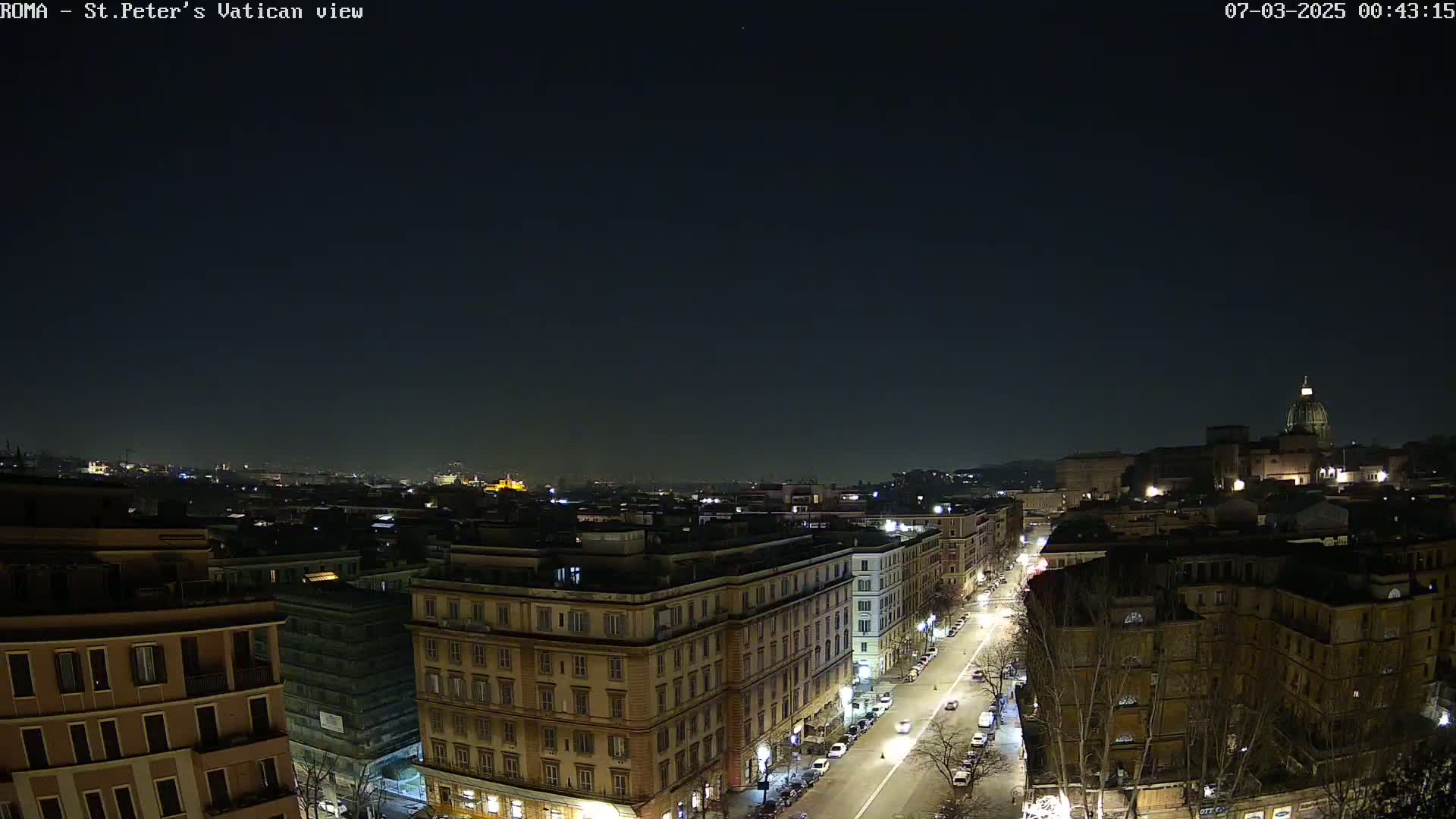 A nighttime, high-angle view of a city street scene with buildings illuminated, under a clear, dark sky.