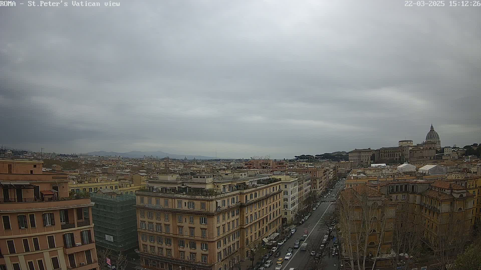 A panoramic view of Rome on an overcast day shows a cityscape extending to the distant mountains, with St. Peter's Basilica visible in the background.