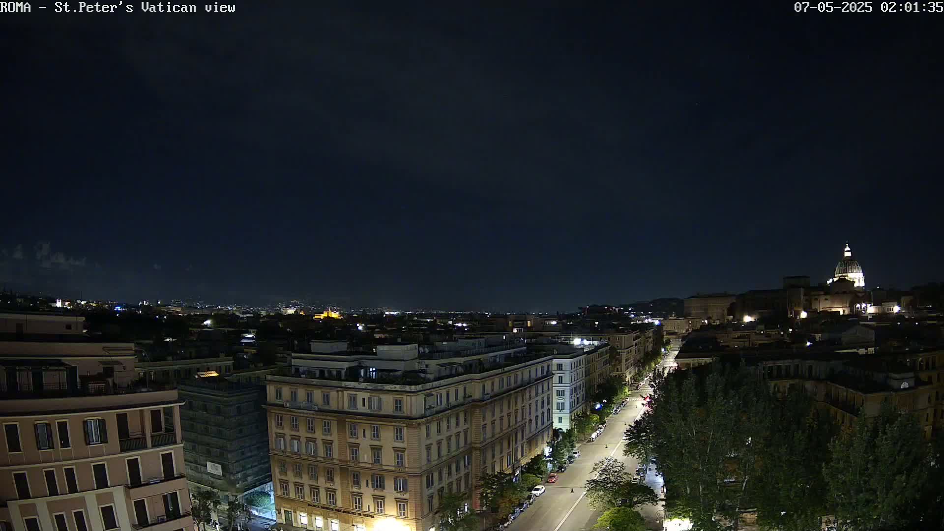 A nighttime view of a city with buildings and a street illuminated under a dark, clear sky.