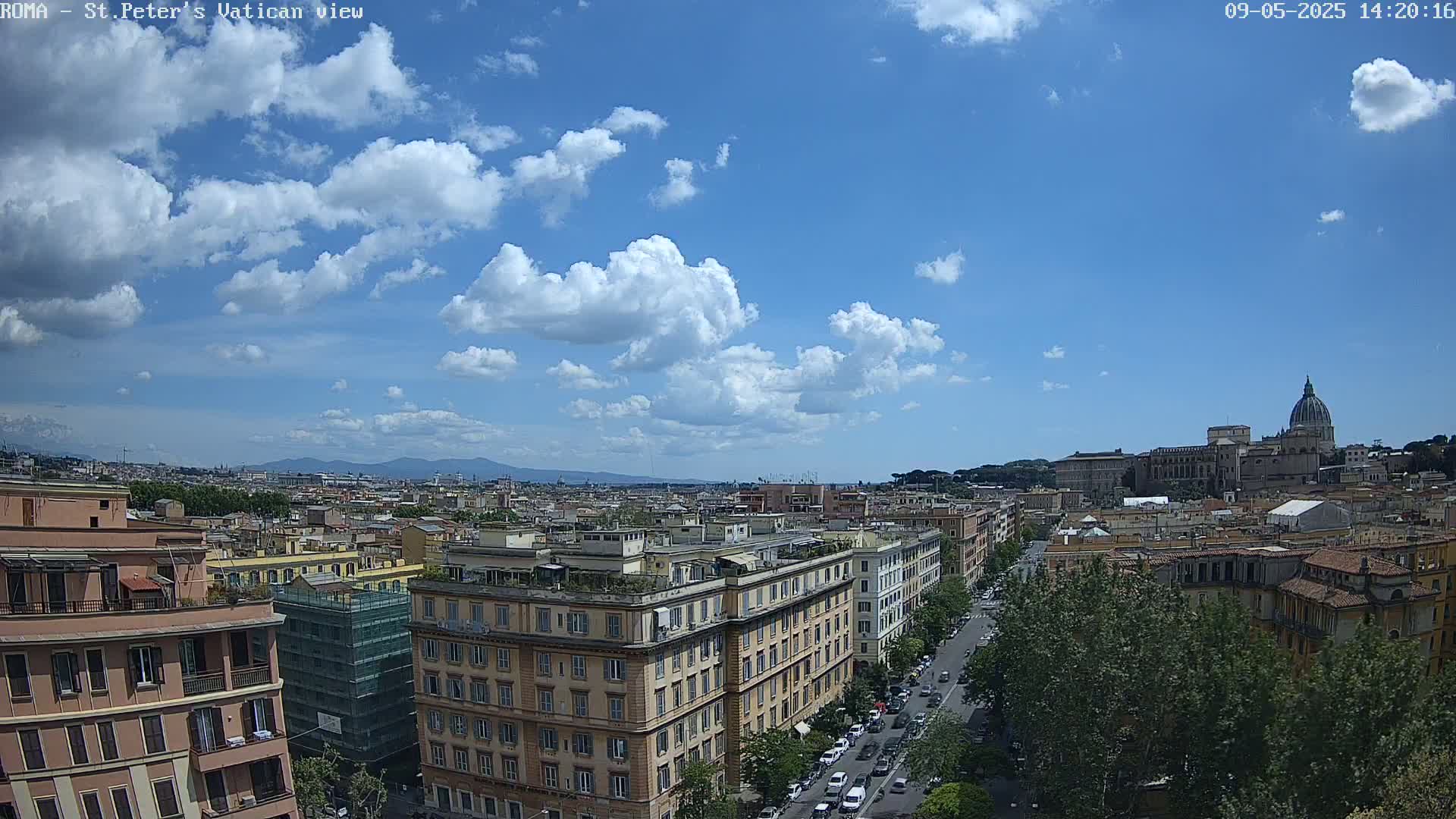 A partly cloudy blue sky overlooks a cityscape of Roman buildings, a street with cars, and the dome of St. Peter's Basilica in the distance.