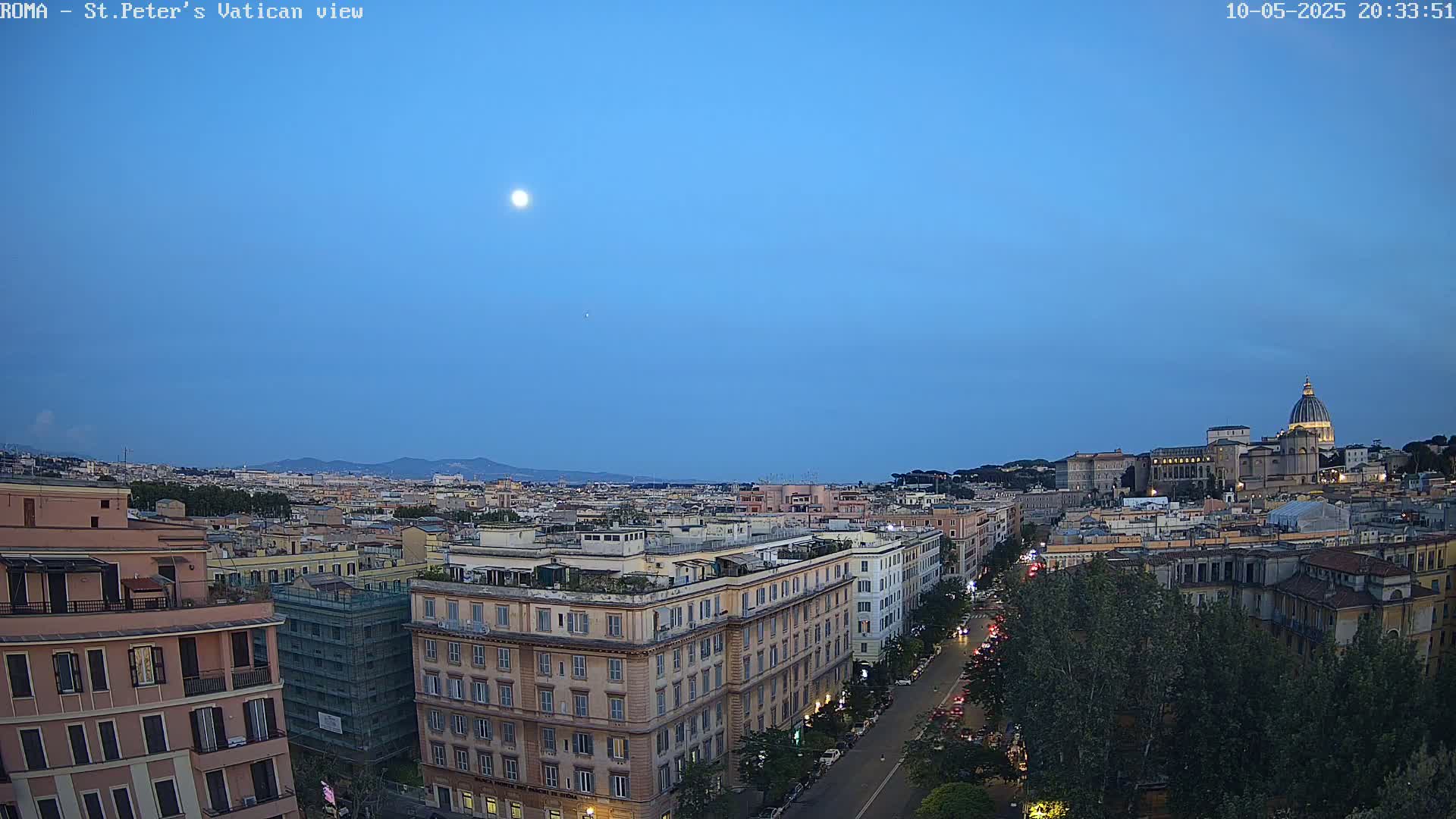 A nighttime view of Rome, Italy, shows a city skyline under a clear, twilight sky with a visible moon.