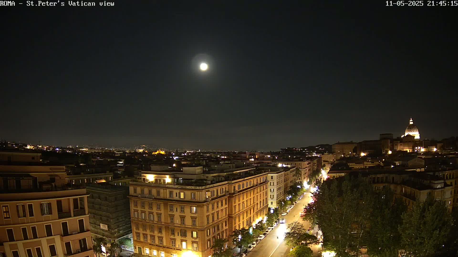A nighttime cityscape with a bright moon overhead, illuminated buildings, and a street with cars.