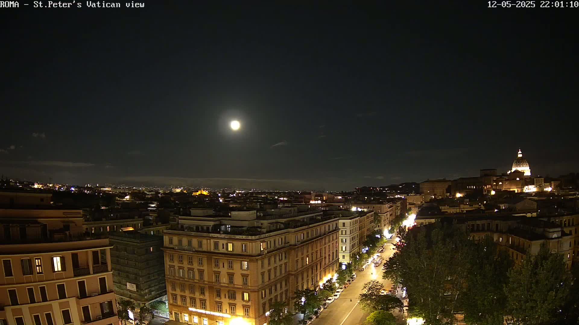 A nighttime cityscape view shows a bright moon in the sky over a city with illuminated buildings and streets, including a large dome in the distance.
