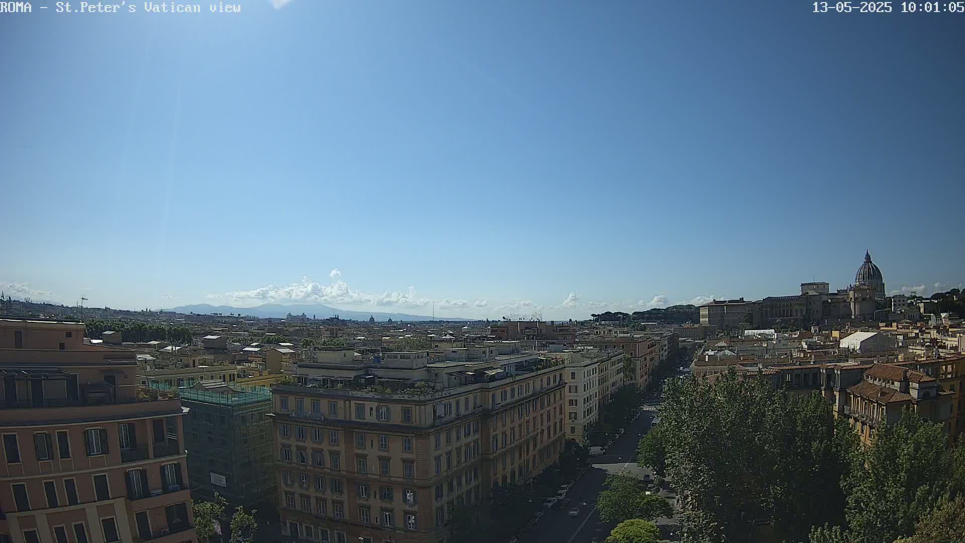 A sunny cityscape view shows St. Peter's Basilica in the distance, with a partly cloudy sky above a city of mostly tan buildings.