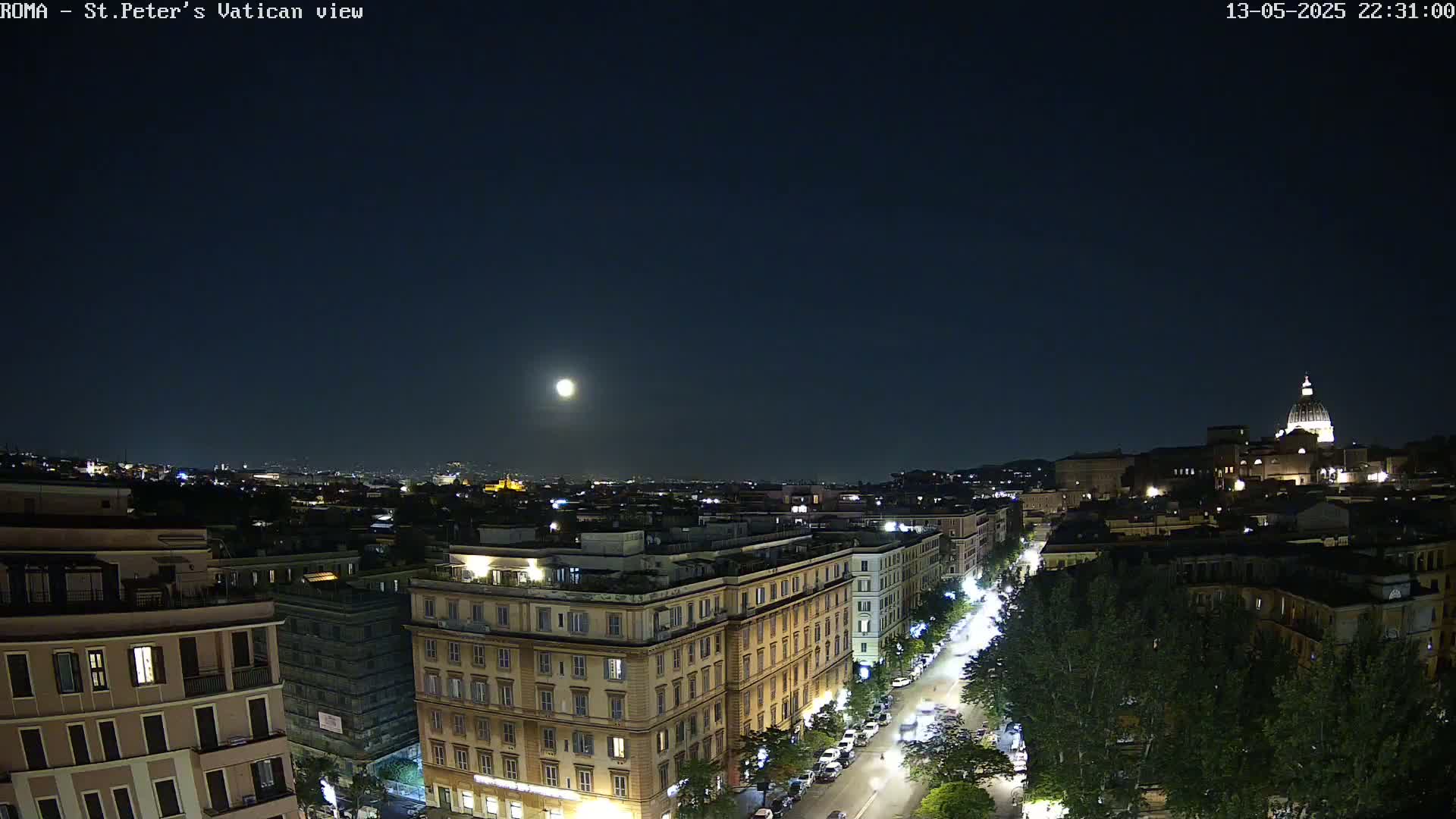 A nighttime cityscape with a bright moon in the sky shows a street lined with trees and buildings, including a large building with a dome in the distance.