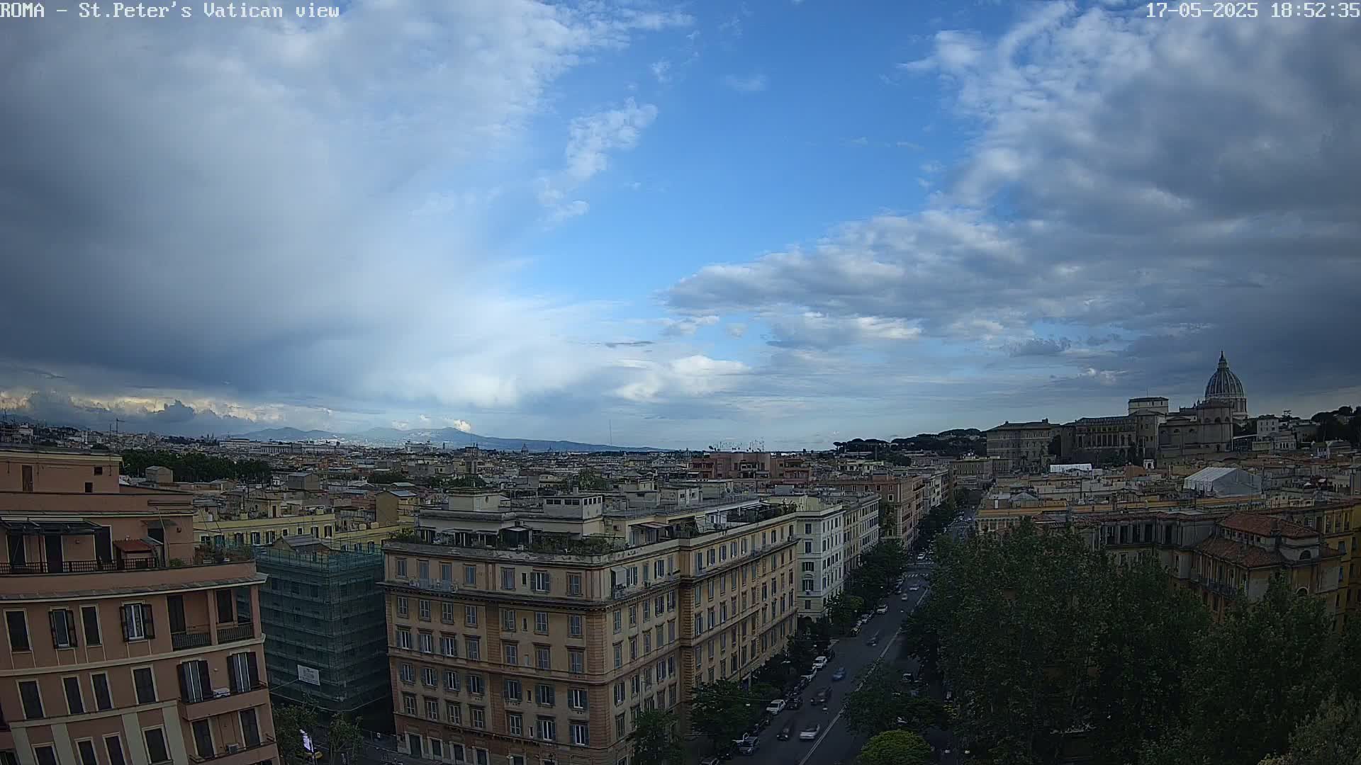 A partly cloudy sky hangs over a cityscape, with the dome of St. Peter's Basilica visible in the distance.